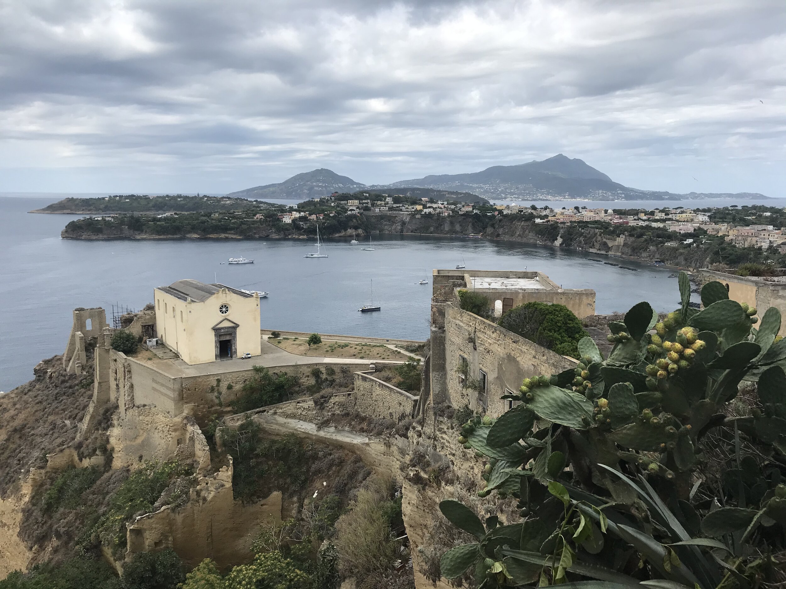 PROCIDA, Napoli. August 5th, 2020. PICTURED: Taken from the town streets above the old prison complex, the curve of Procida island bends dramatically around volcanically-blackened waters.