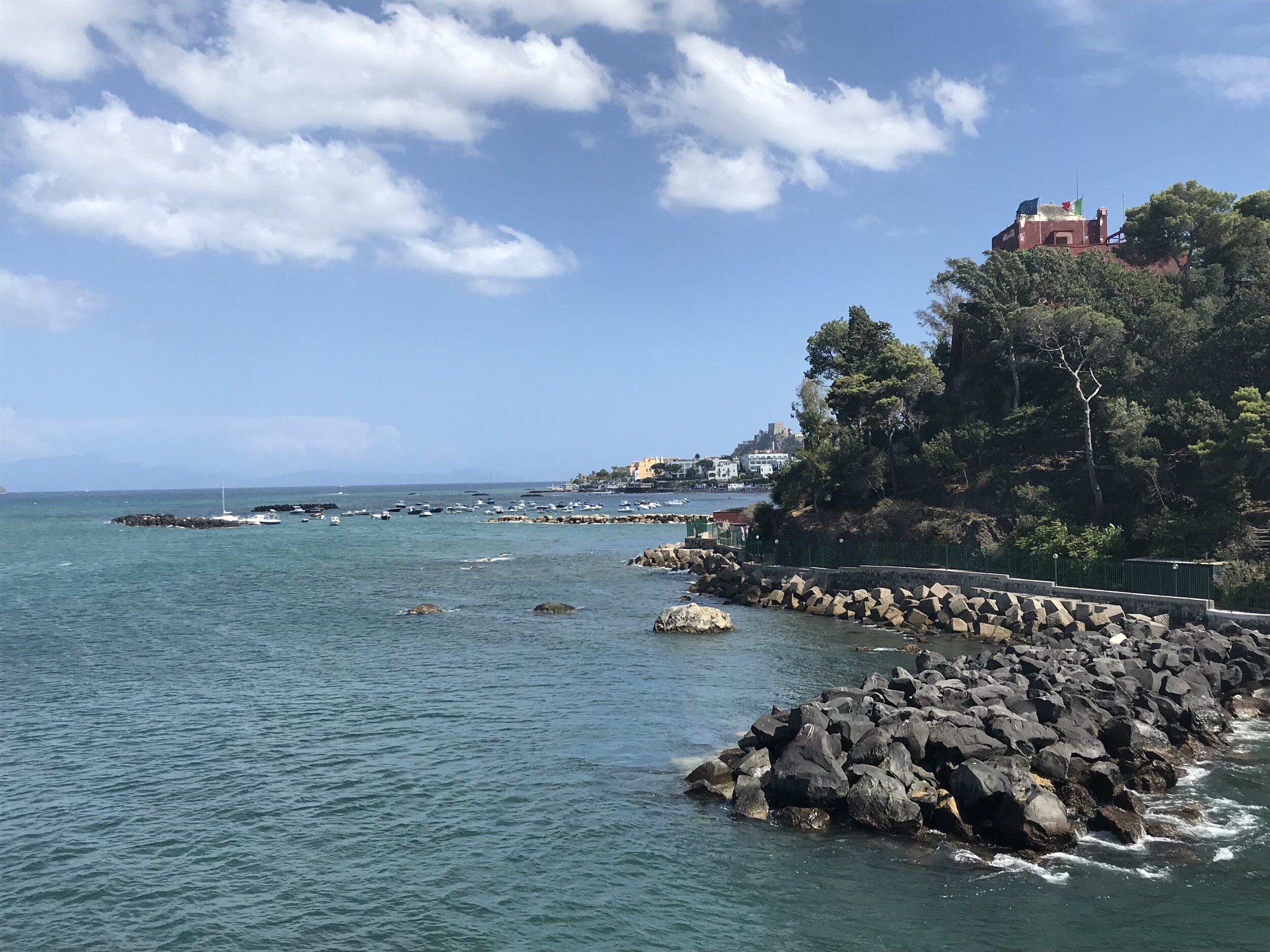  ISCHIA, Napoli. August 5th, 2020. PICTURED: One of the finest hotels on the island repels the light from the glittering sea with its brick red facade at the entrance to the Ischia port. 