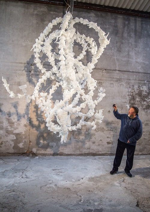 PICTURED: The artist Ai Weiwei with his massive glass-blown sculpture "Blossom Chandelier," in Venice. The large-scale installation bursts with unexpected shapes emanating from white glass flowers to surprise the eye: menacing handcuffs, twitter bir…