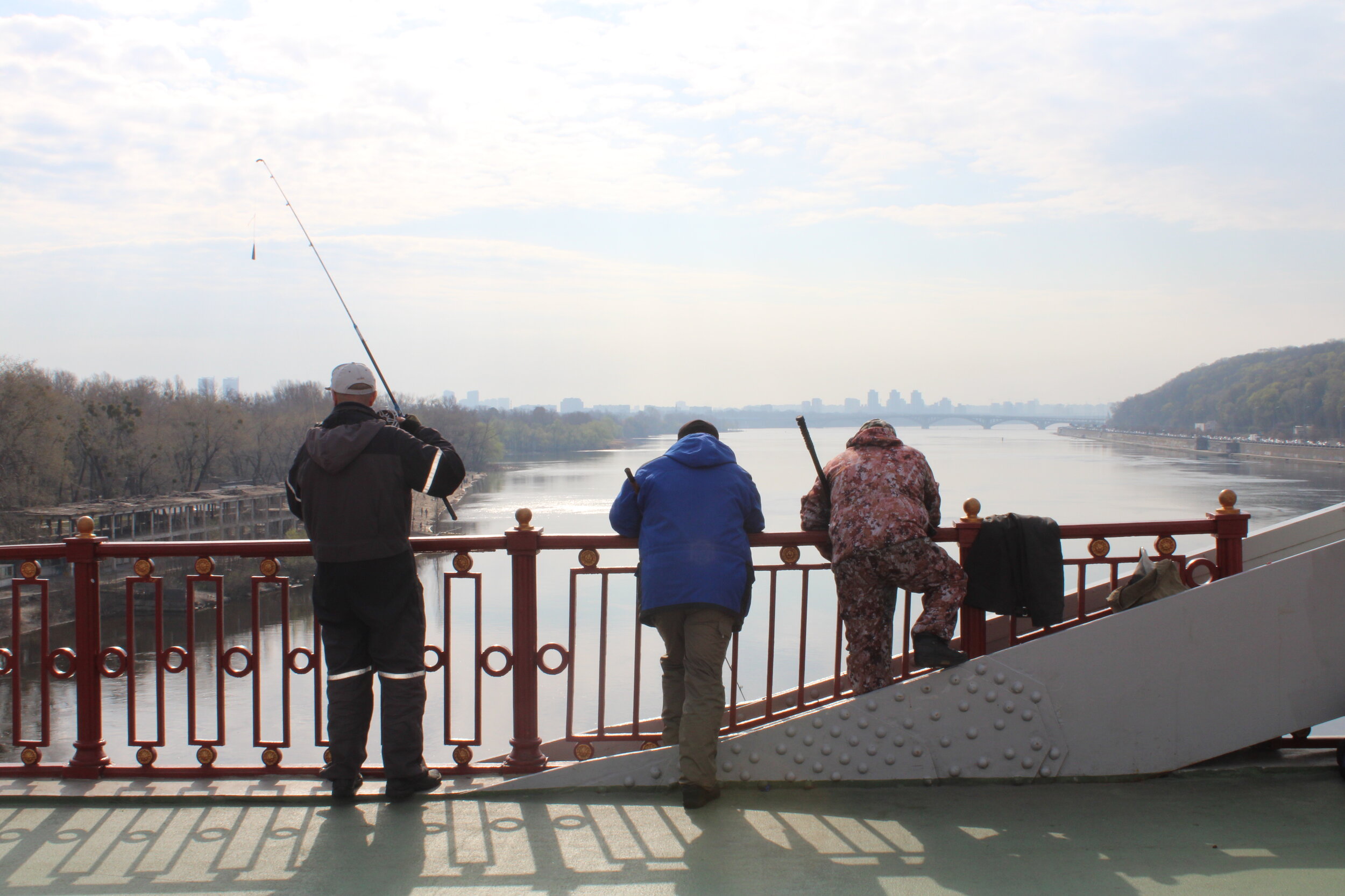 PICTURED: Hobby fishermen enjoying a moment of sun in the cool morning, casting their lines over the pedestrian bridge over the Dnieper.