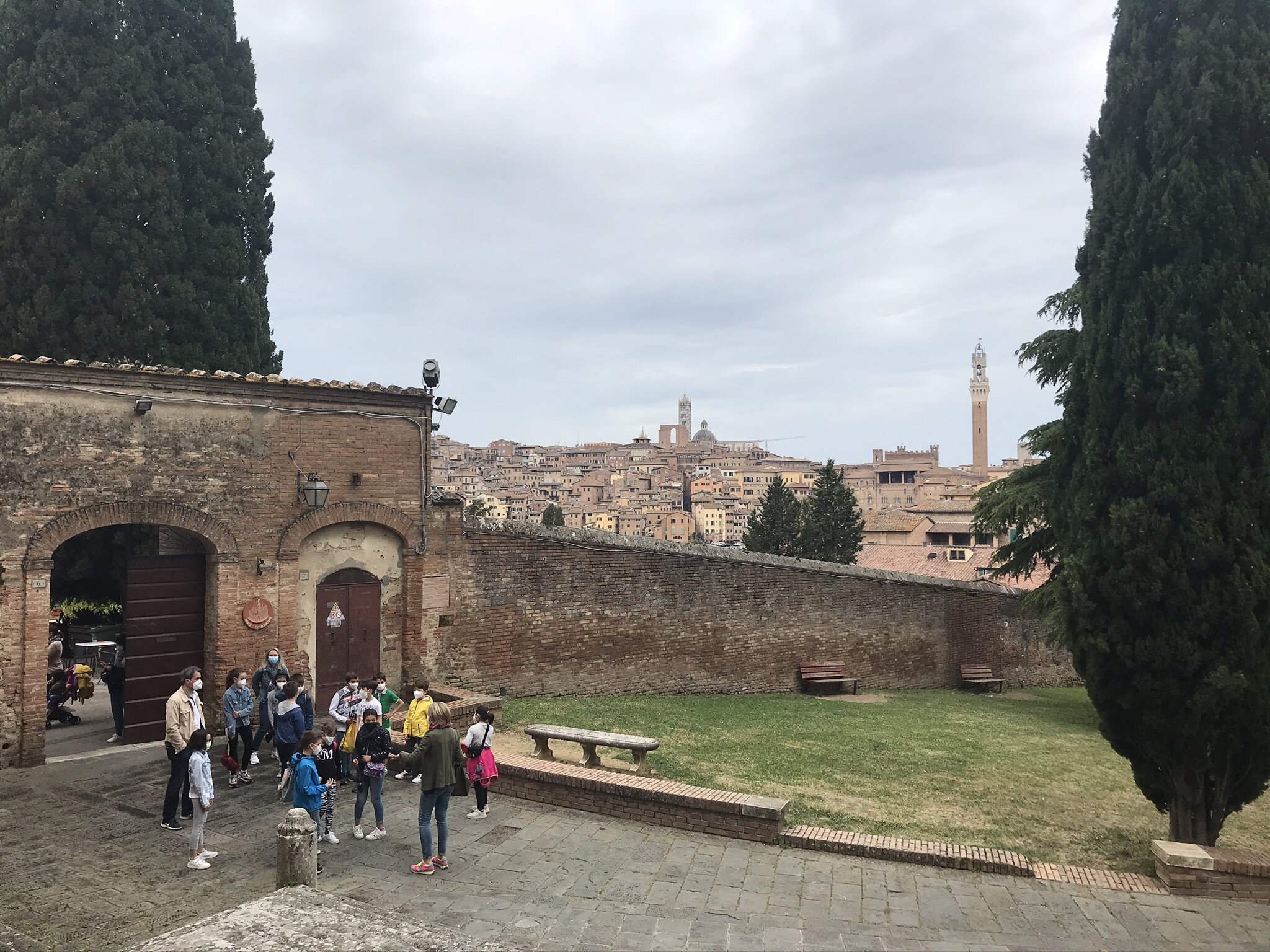 SIENA, Italy. June 4th, 2021. PICTURED: Schoolchildren on a fieldtrip in front of the offices of the Contrada del Valdimontone, or Valley of the Ram, with Siena’s Duomo, Torre di Mangia, and Piazza del Campo all visible in the background.