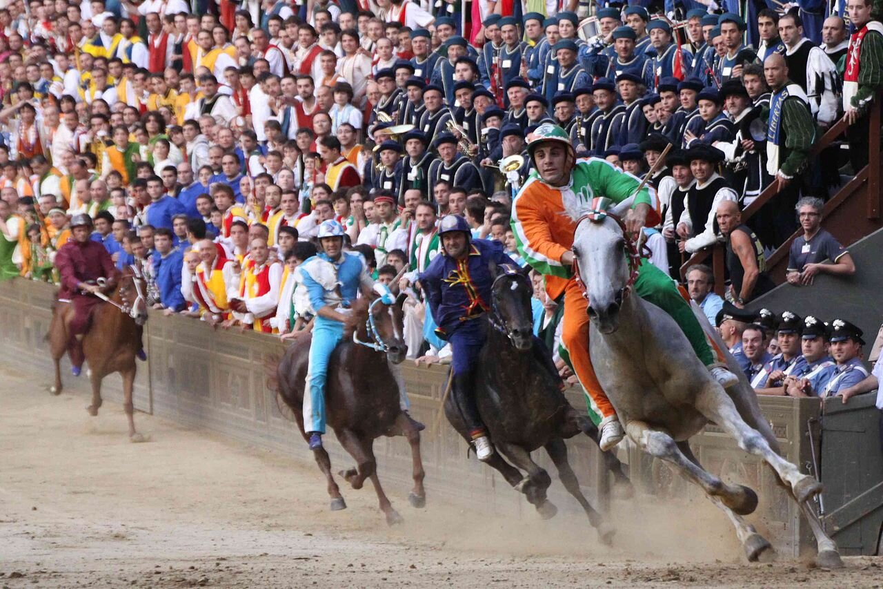 PICTURED: An image of the Palio from July 2nd, 2009. The lead rider, Silvano Mulas, wears the colors of the Contrada della Selva, or Society of the Forest. Photo credit: Roberto Vicario. CC 3.0.