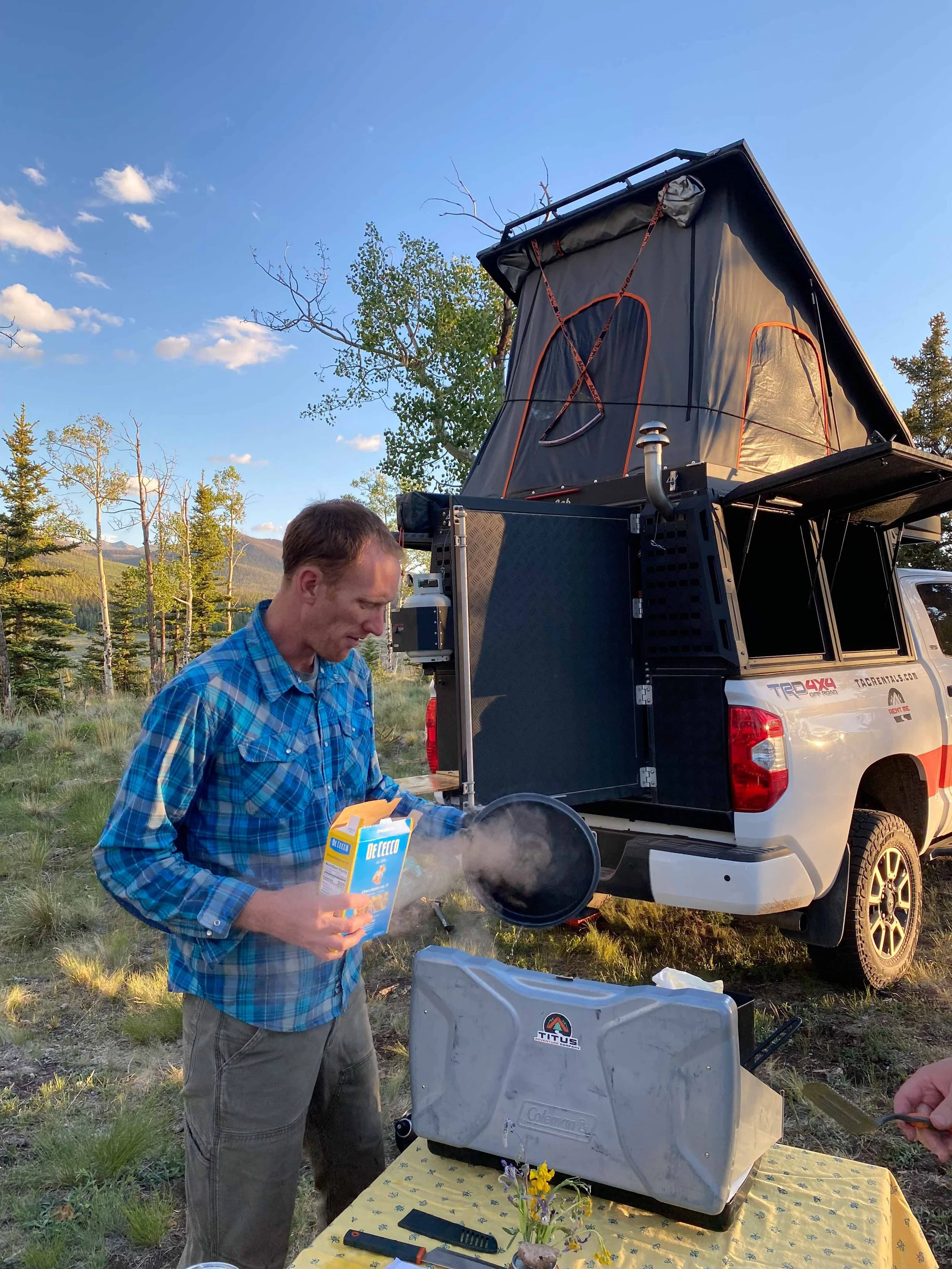 Travis Titus, of Titus Adventure Company, cooking on a camping stove, standing behind one of his 4x4 rentals near Denver, CO.
