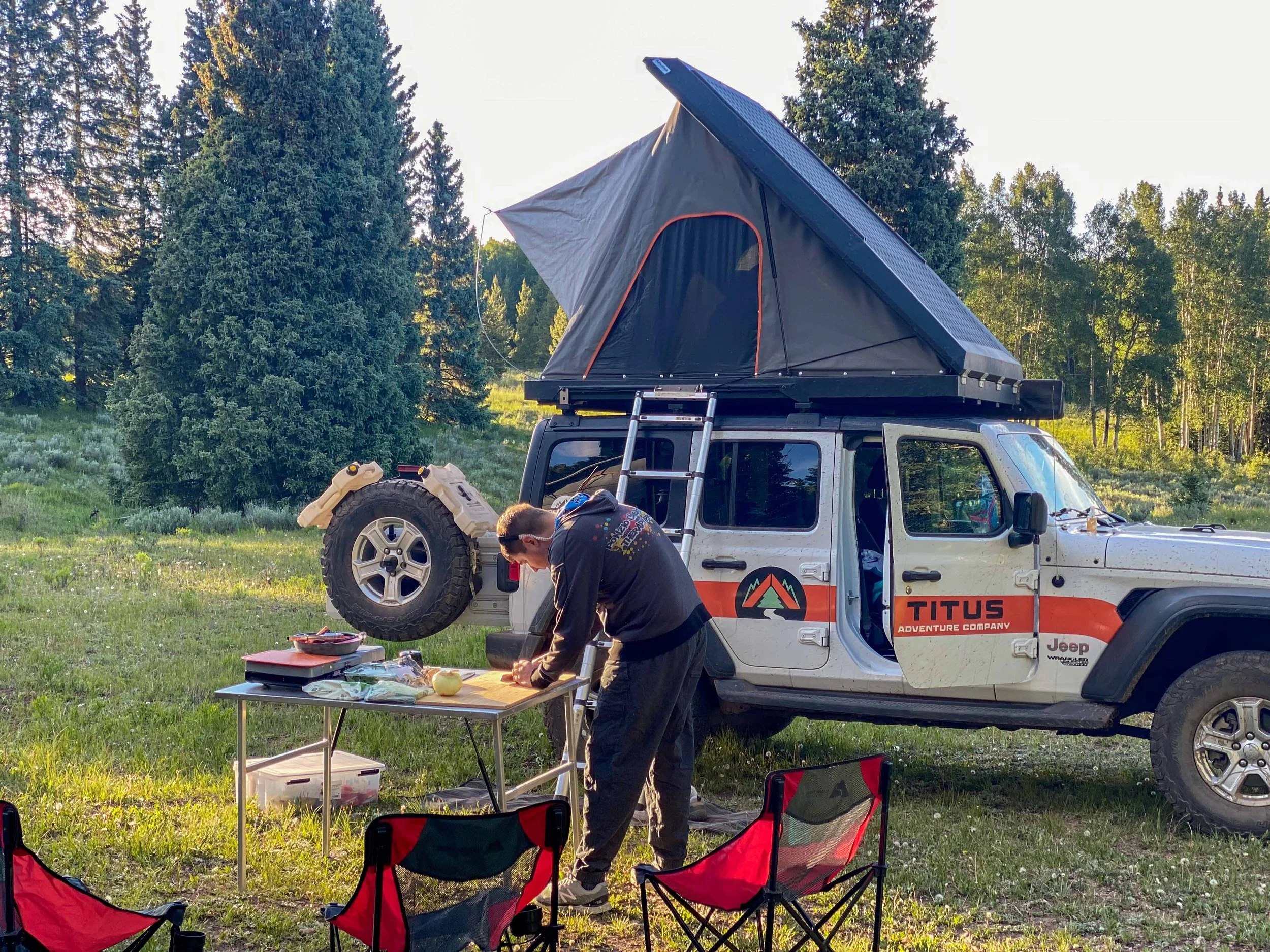 Man prepping to cook at camp, standing in front of a Titus Adventure Company 4WD rental with pop-up, rooftop tent.