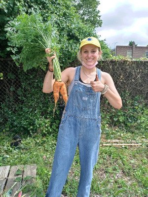 photo: woman in overalls holding up carrots