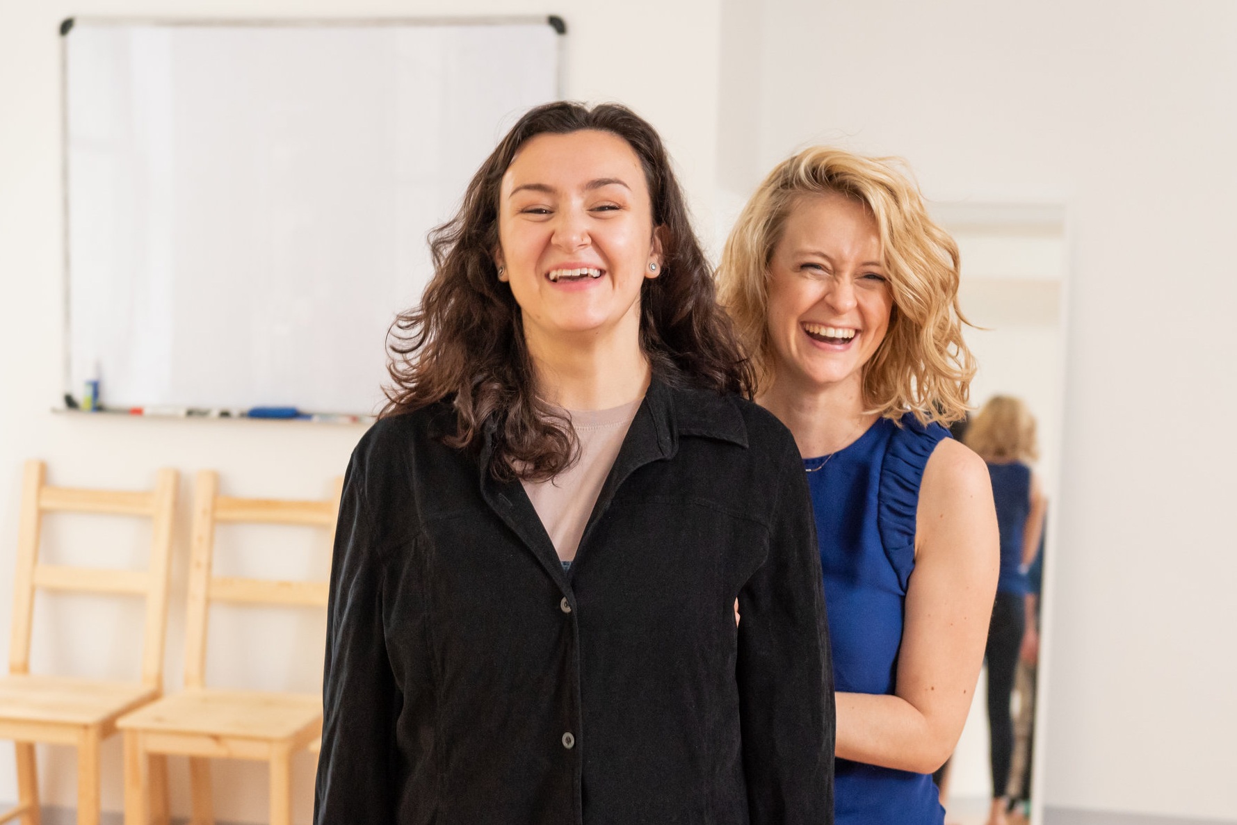 Dana Calvey stands behind an Alexander Technique Acting student providing hands on guidance. They laugh.