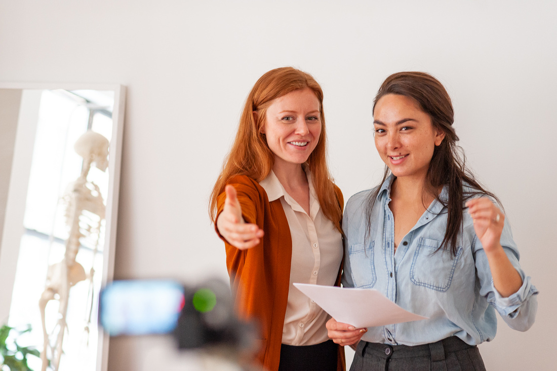 Holly Cinnamon, working actor and Alexander technique teacher, teaches an acting student on camera audition technique. She stands to the left of the student who is holding audition sides. Holly gestures to teh camera.