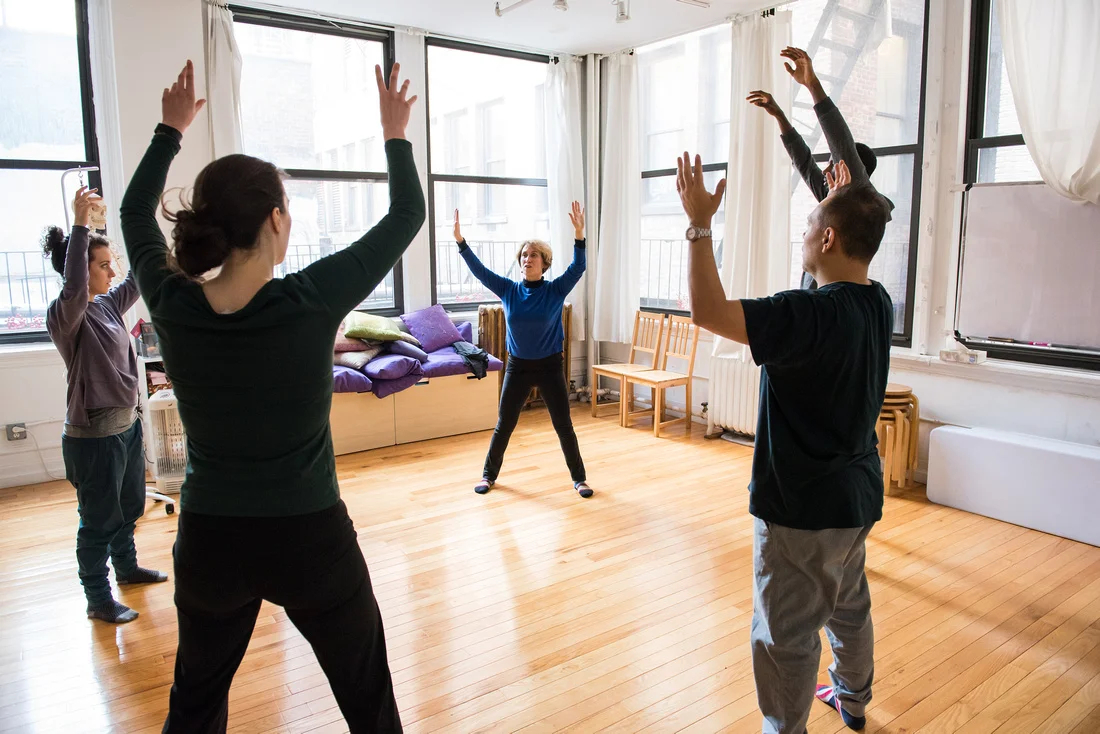 Belinda Mello, Master Alexander Technique Teacher helps an actor through a series of floor exercises meant to provide a means for the actor to use their whole body as one. The actor holds a band of fabric in the air and Belinda gently holds the actors knees giving her direction.