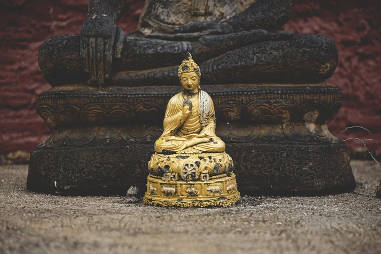 A golden Buddha statue sits on the ground in front of a larger Buddha statue.