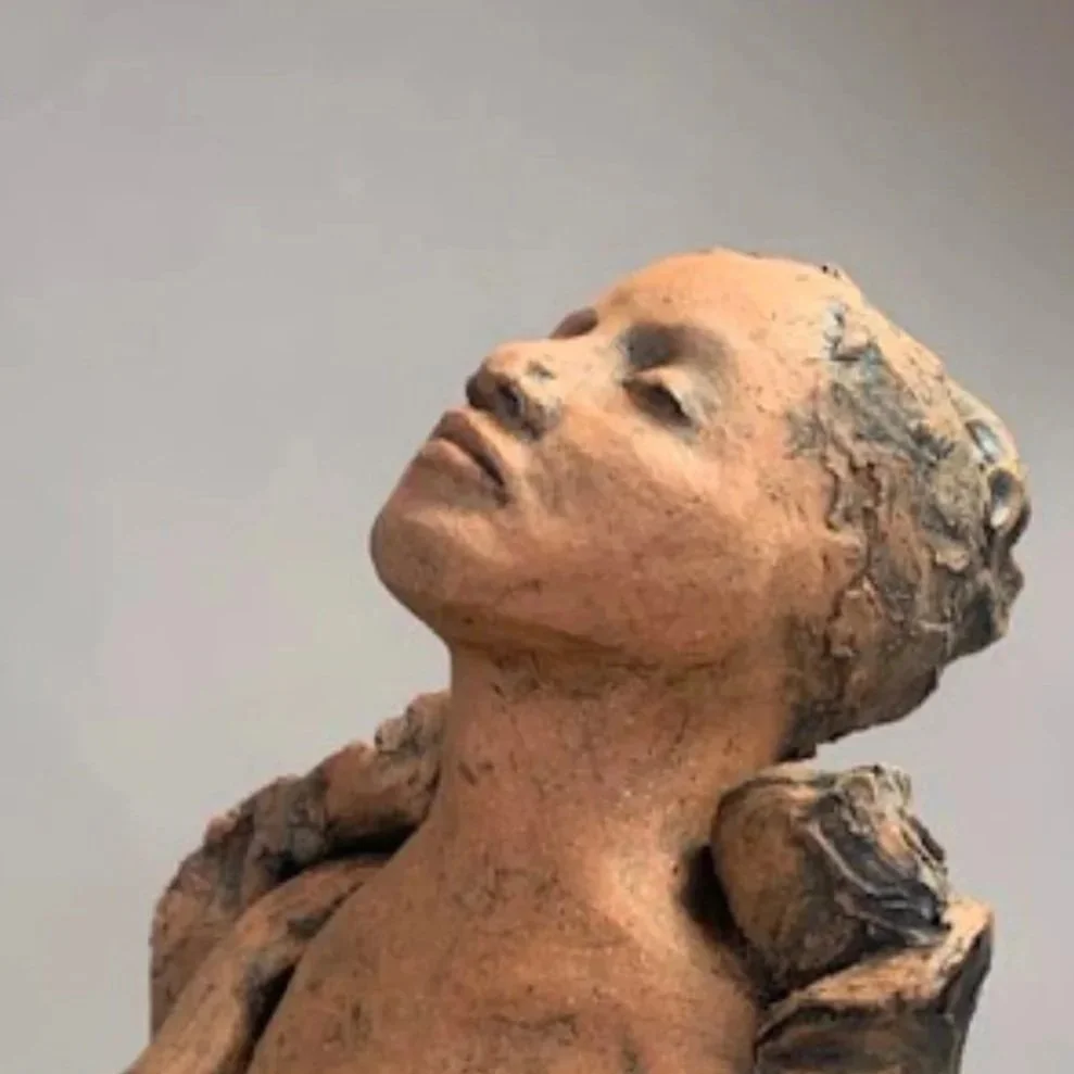 Sculpture of a woman’s head and upper body emerging from a textured, rock-like base.