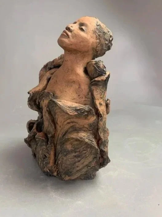 Sculpture of a woman’s head and upper body emerging from a textured, rock-like base.