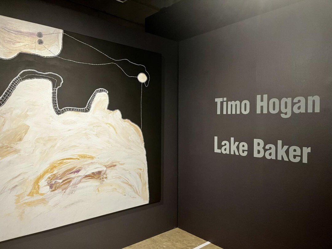 Timo Hogan paints Lake Baker, a large salt lake to the north west of traditional Spinifex Lands.

Lake Baker is guarded by a powerful Wati Wanampi (Water Serpent Man) who resides in a rockhole to the edge of the lake and must be pacified by different