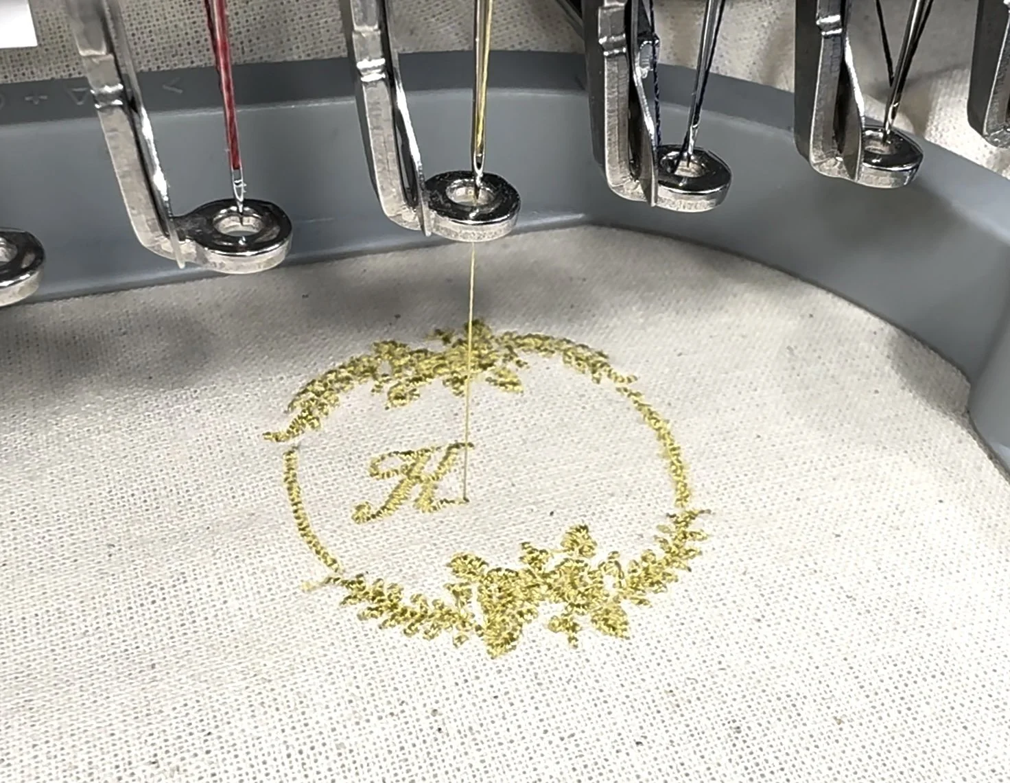 Close-up of embroidery thread sewing a monogrammed design on white fabric using a computerized embroidery machine.