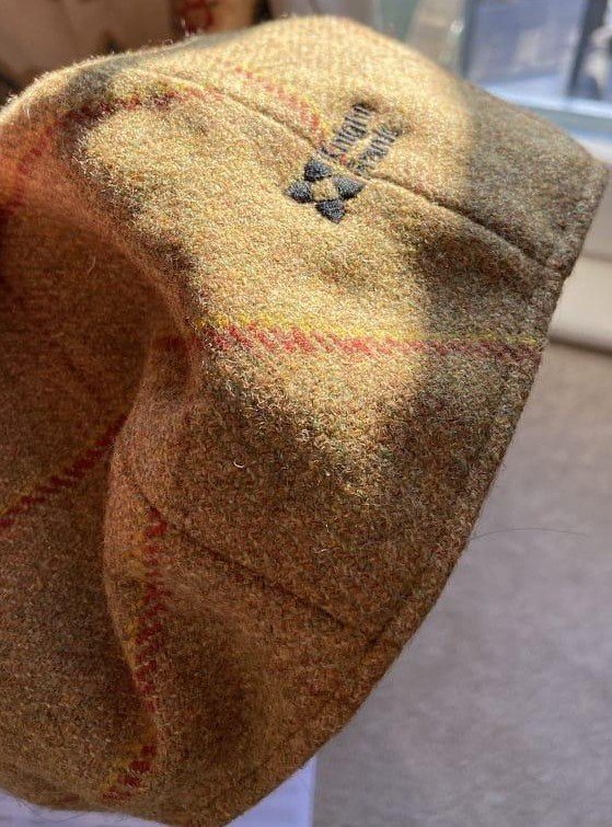 Close-up of a beige cloth item with red and yellow stitching, showing a small embroidered logo and some partially visible text.