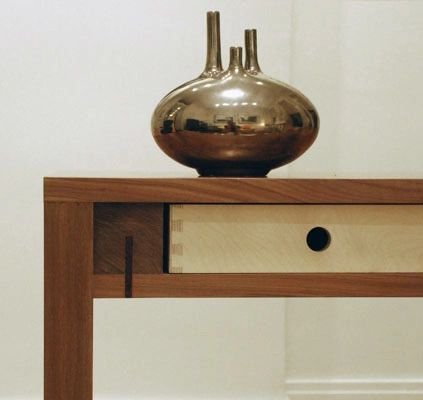 Walnut side table with exposed dovetail joinery and a minimalist drawer design, blending craftsmanship and function. The contrasting wood tones and clean geometric form create a striking balance of simplicity and detail.