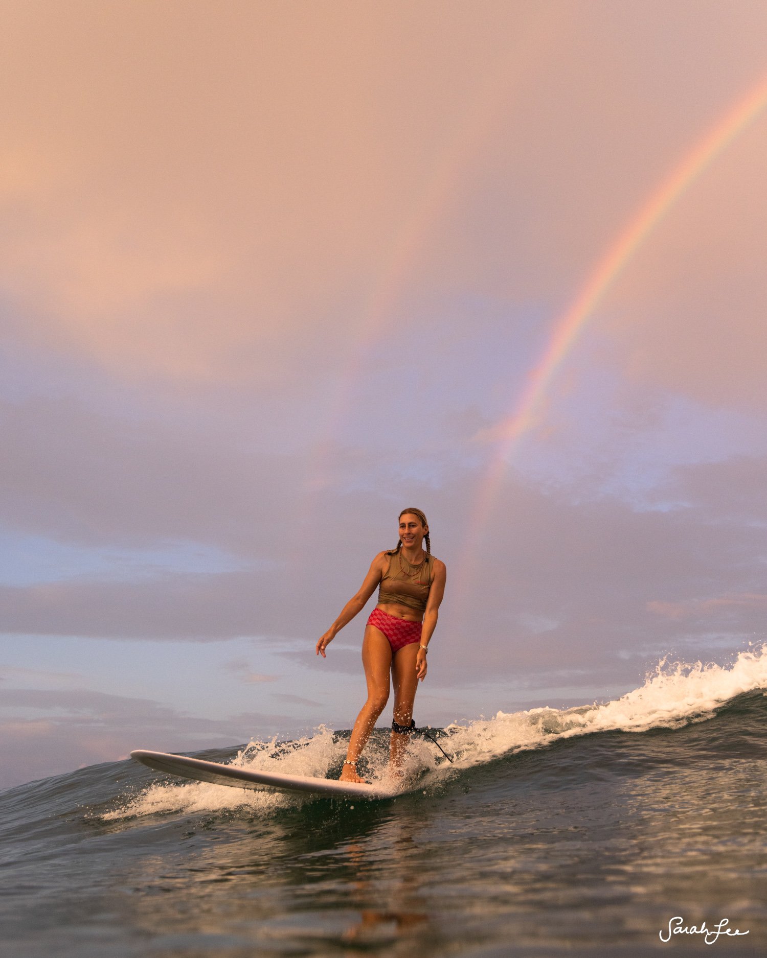 Female surfer surfing under a double rainbow