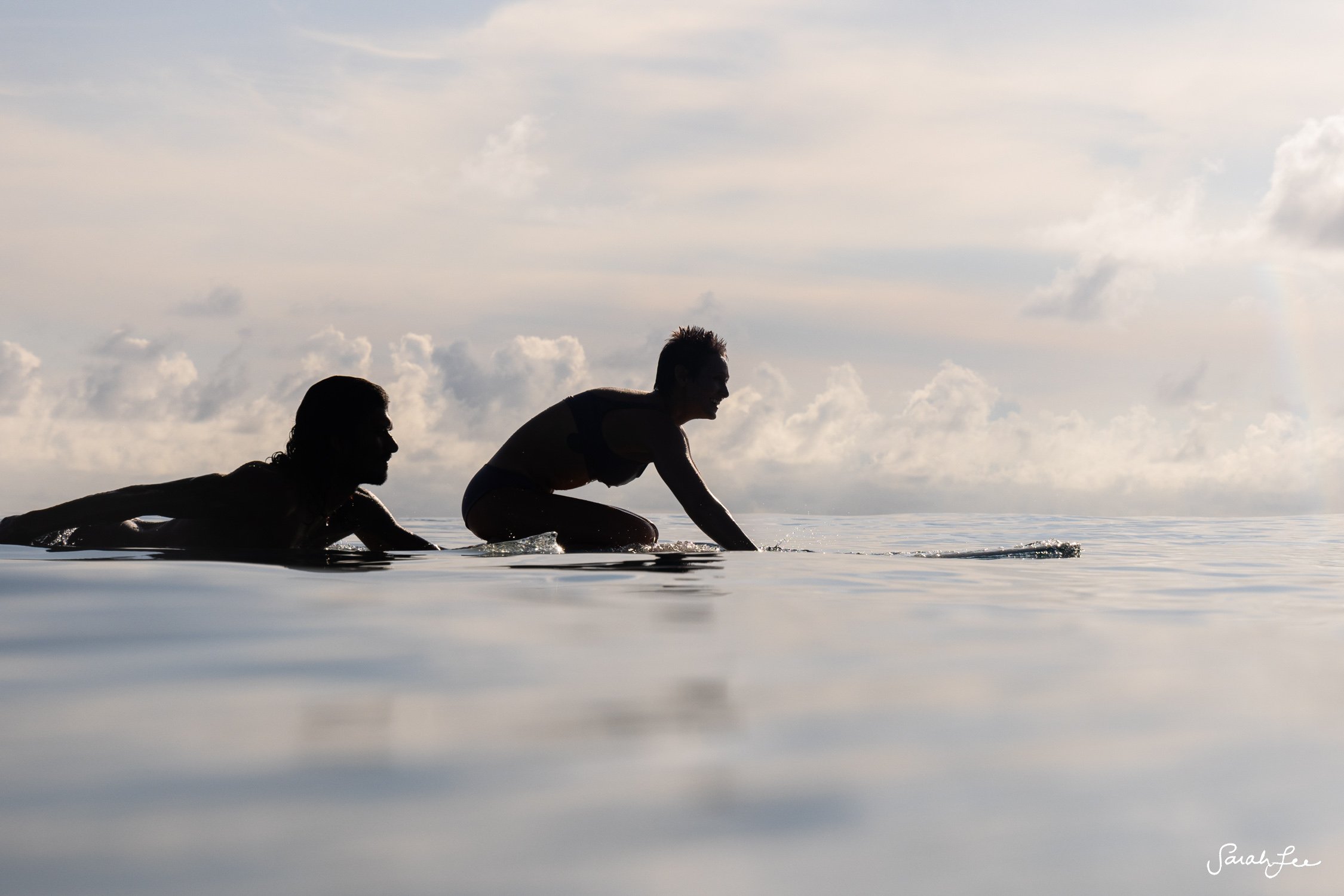 Two silhouetted surfers paddling out at sunrise