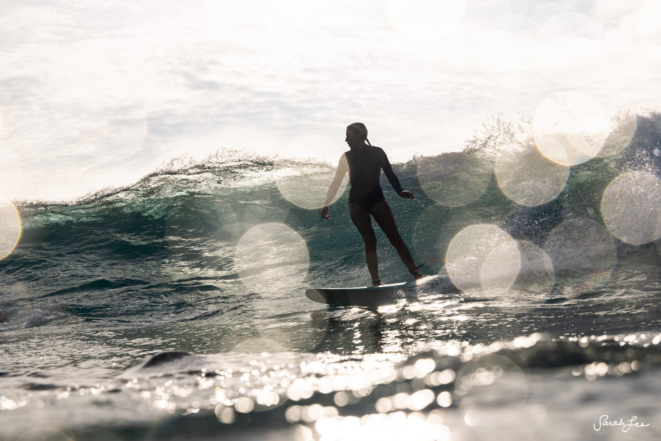 Silhouette of female surfer with water spots and sun flares.