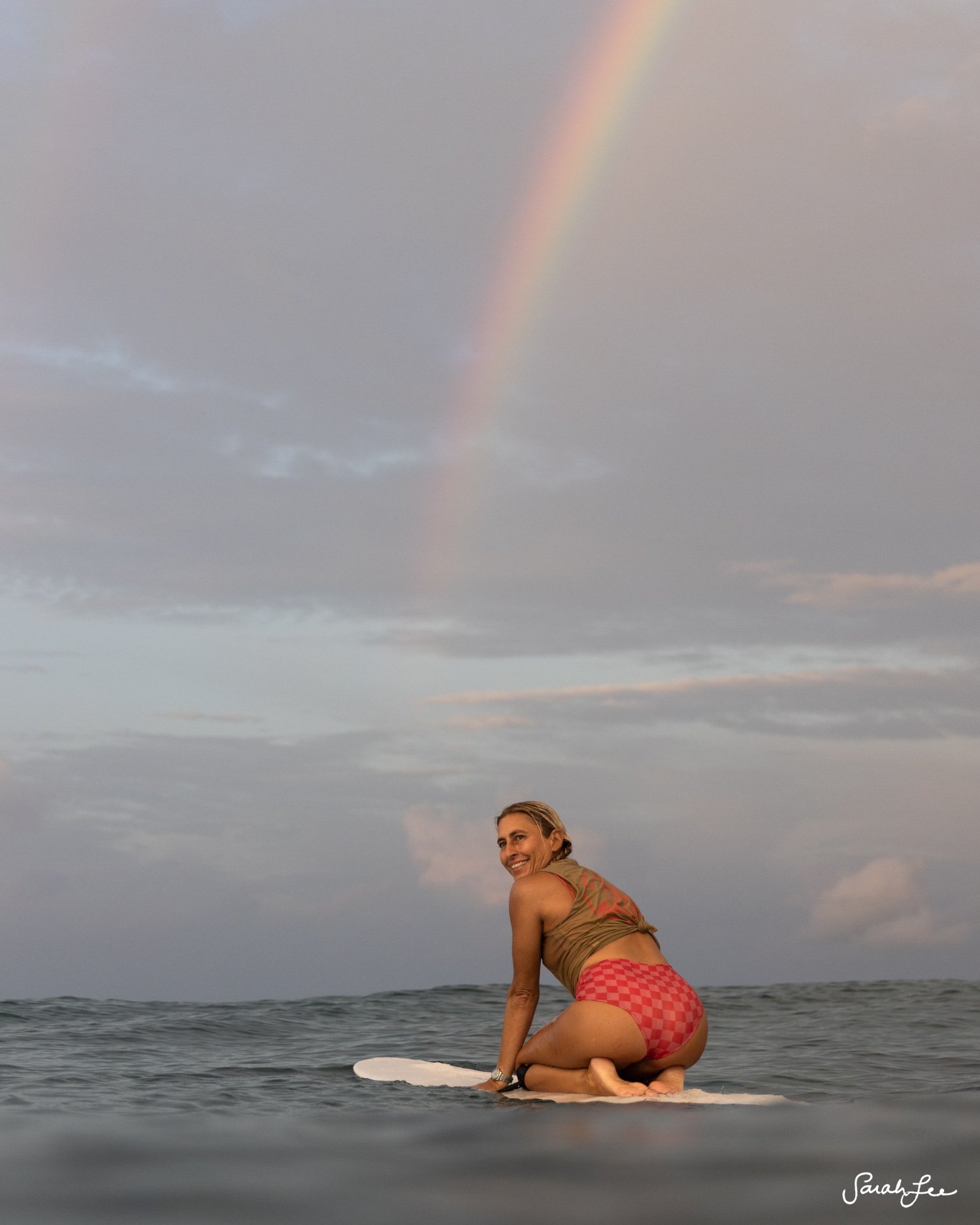 Knee paddle smile under Double Rainbow on a long board surfboard