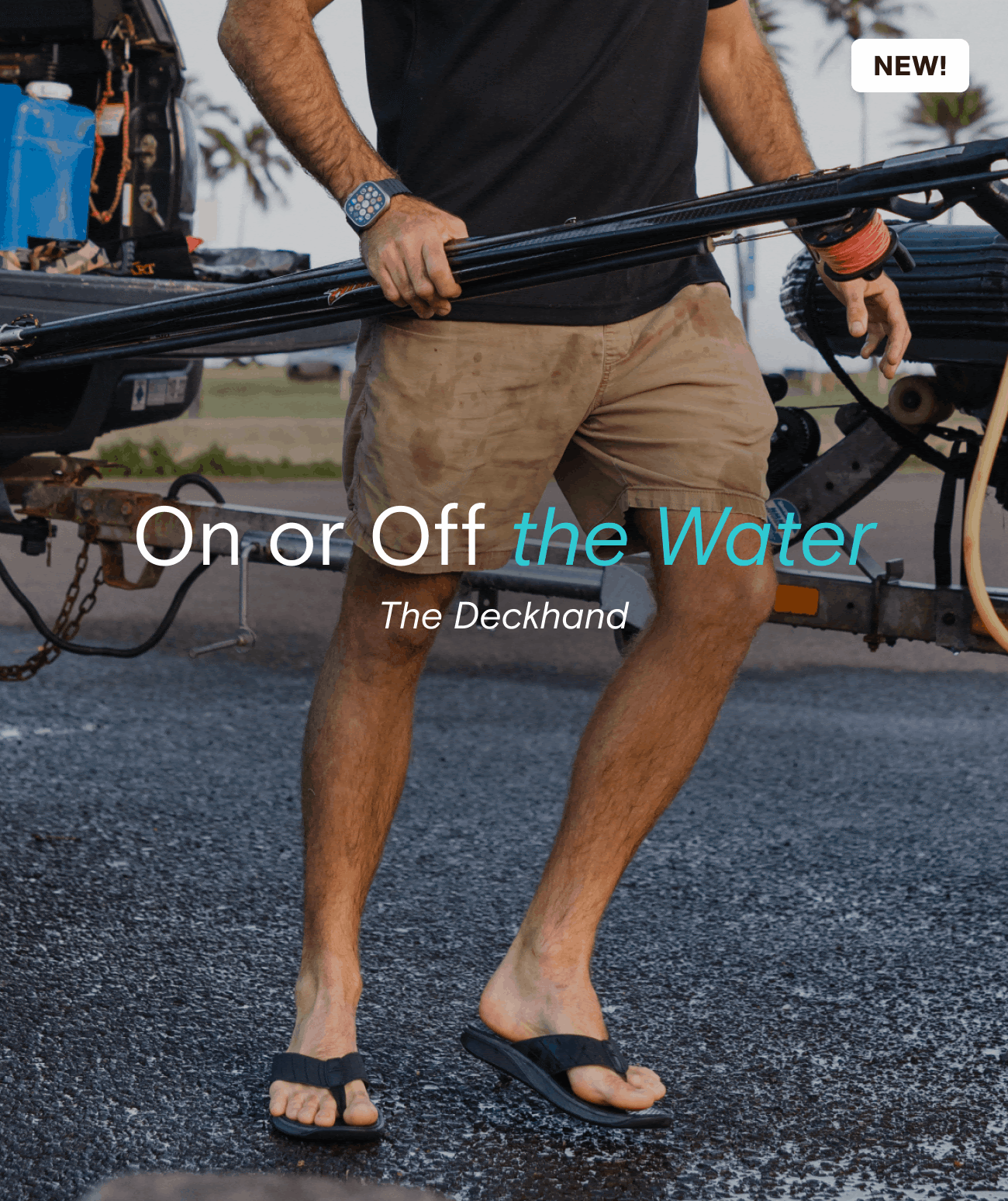 A man holding a kayak paddle standing next to a kayak trailer, wearing tan shorts, flip-flops, and a watch, with a background of palm trees and a partly cloudy sky.