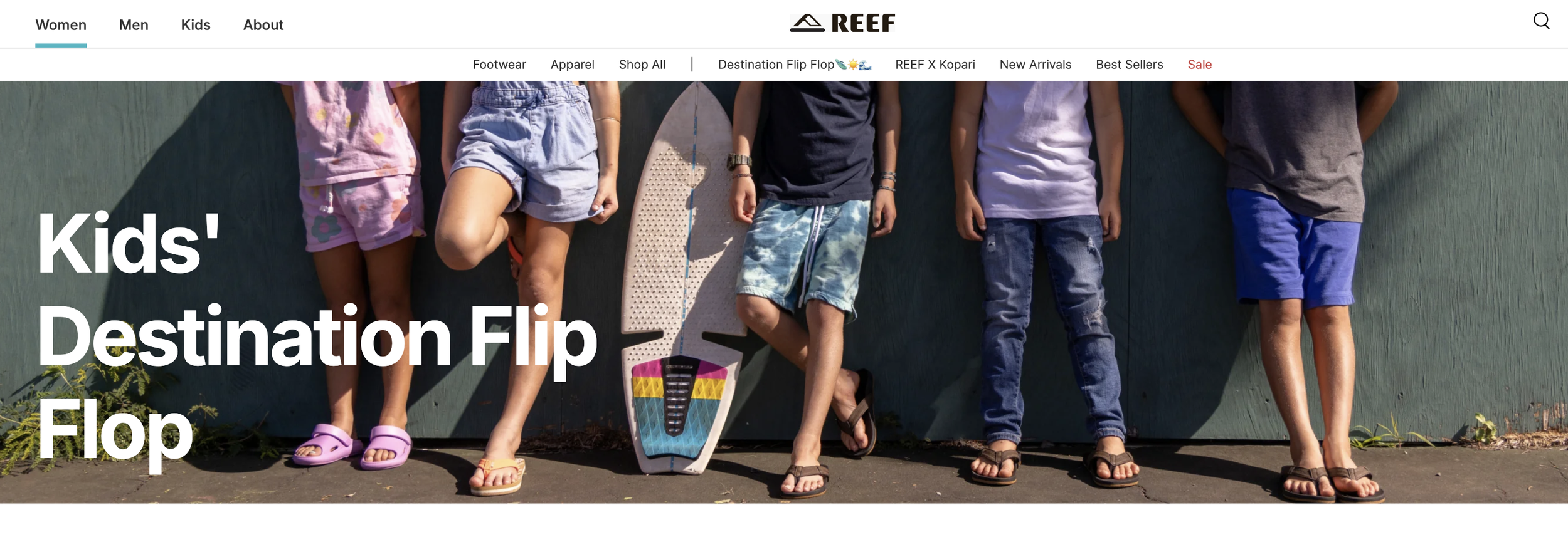 Group of children standing against a green wall, wearing casual summer clothes, with some holding skateboards.