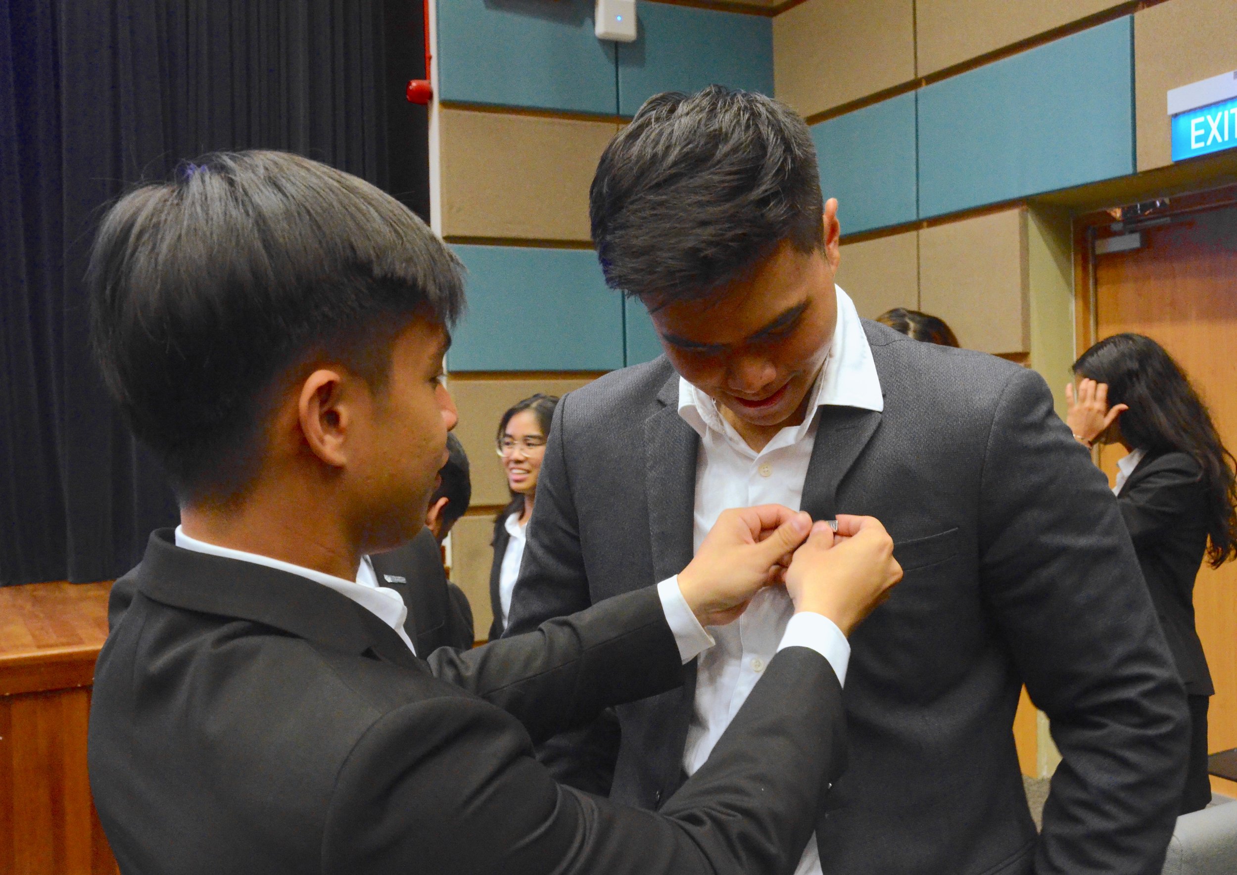 An OGL pinning the NUS Law badge on his freshman