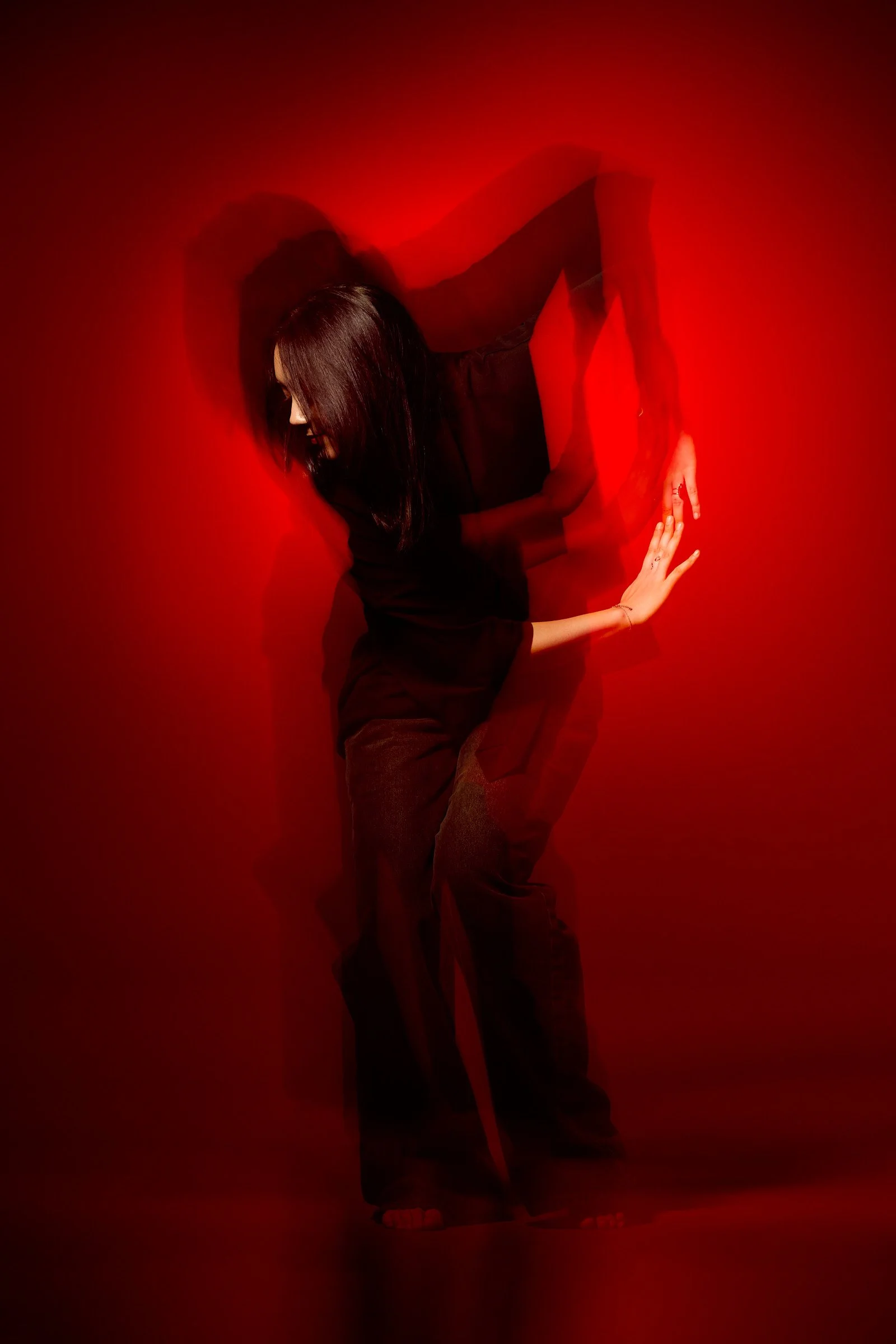 A woman with brown hair dancing in a dark room with red light effects.