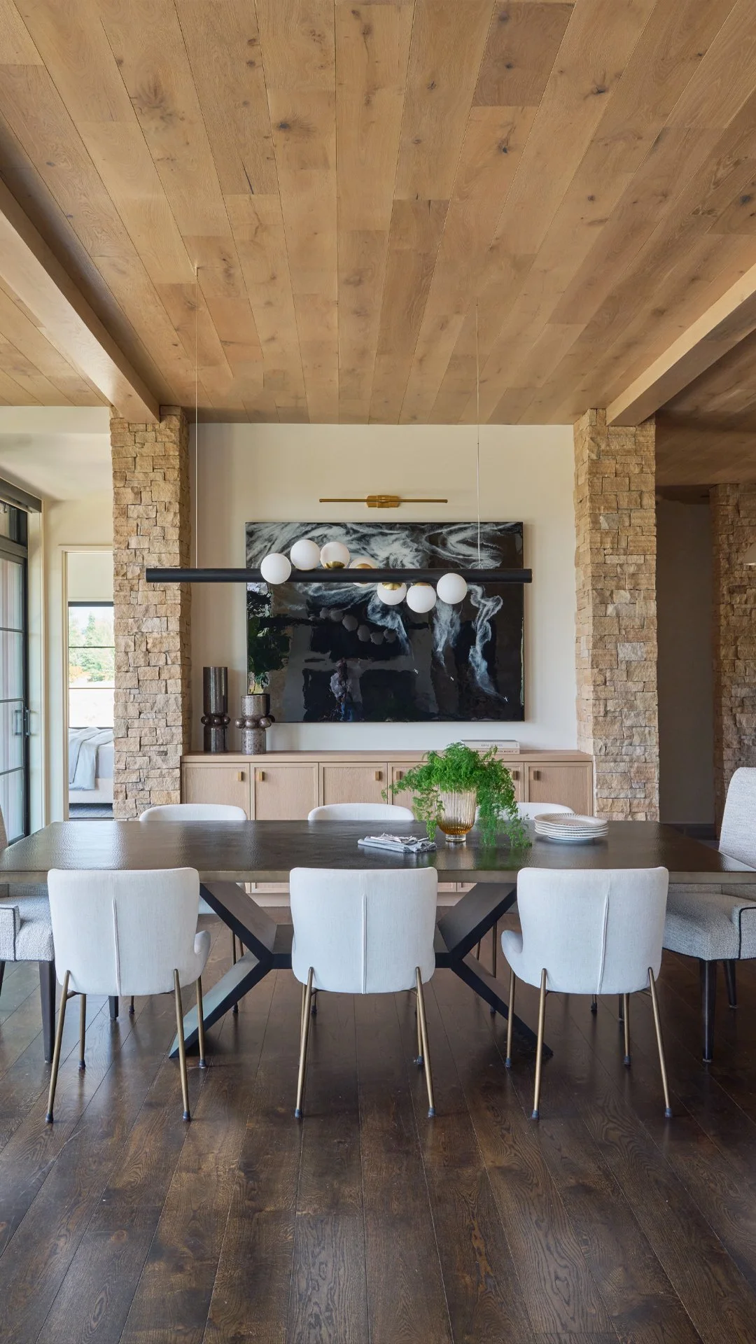 Dining room with custom hammered brass table, white chairs, stone columns and linear chandelier