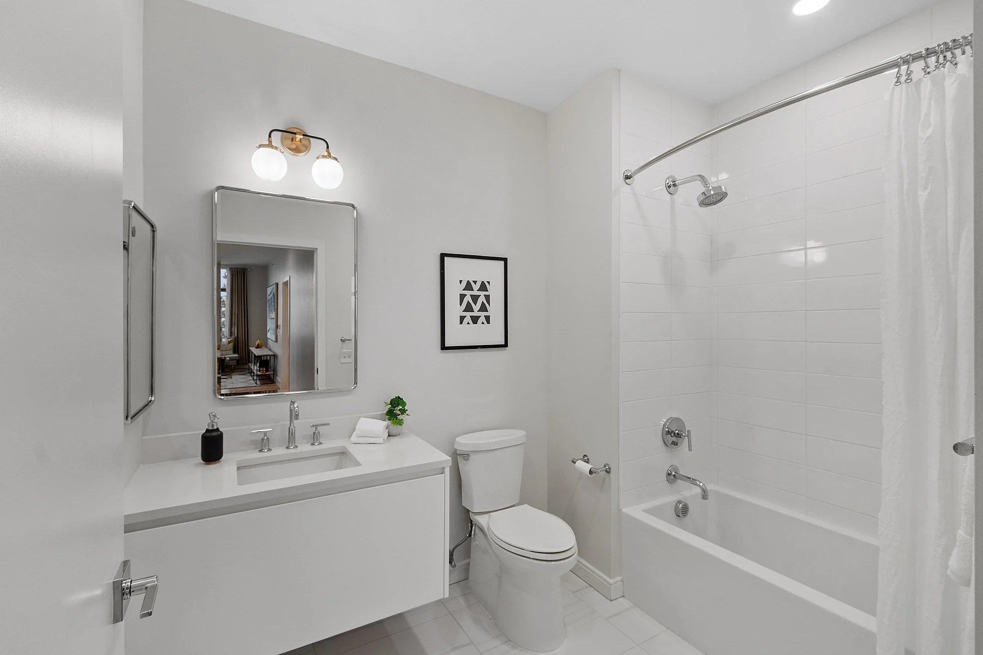 Modern bathroom with white walls, vanity, mirror, toilet, and bathtub with shower, decorated with black artwork and minimal accessories.