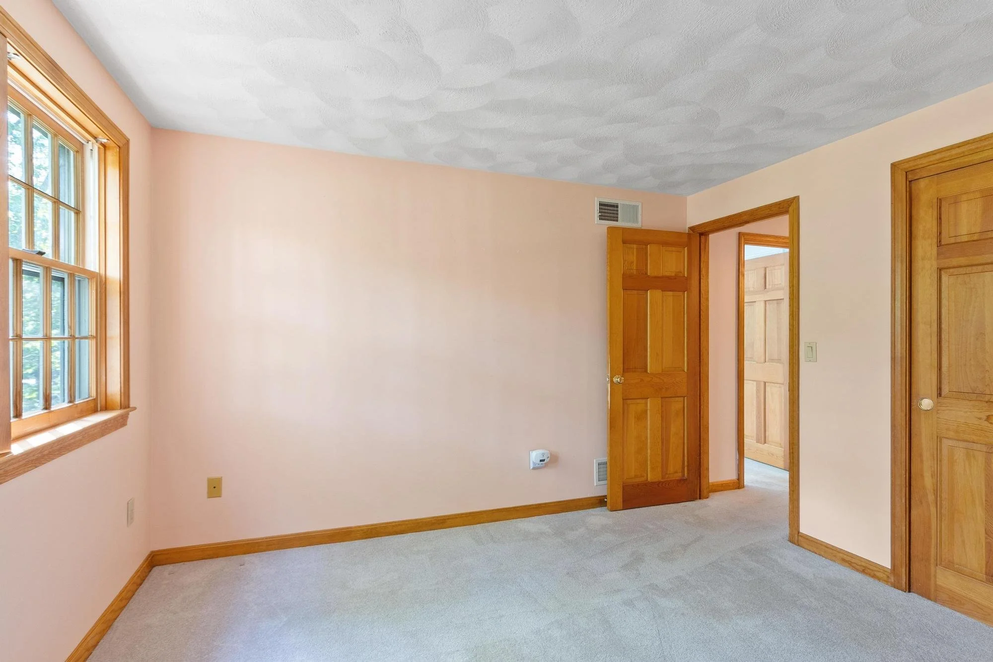Empty room with a window, wooden doors, beige walls, and carpeted flooring.