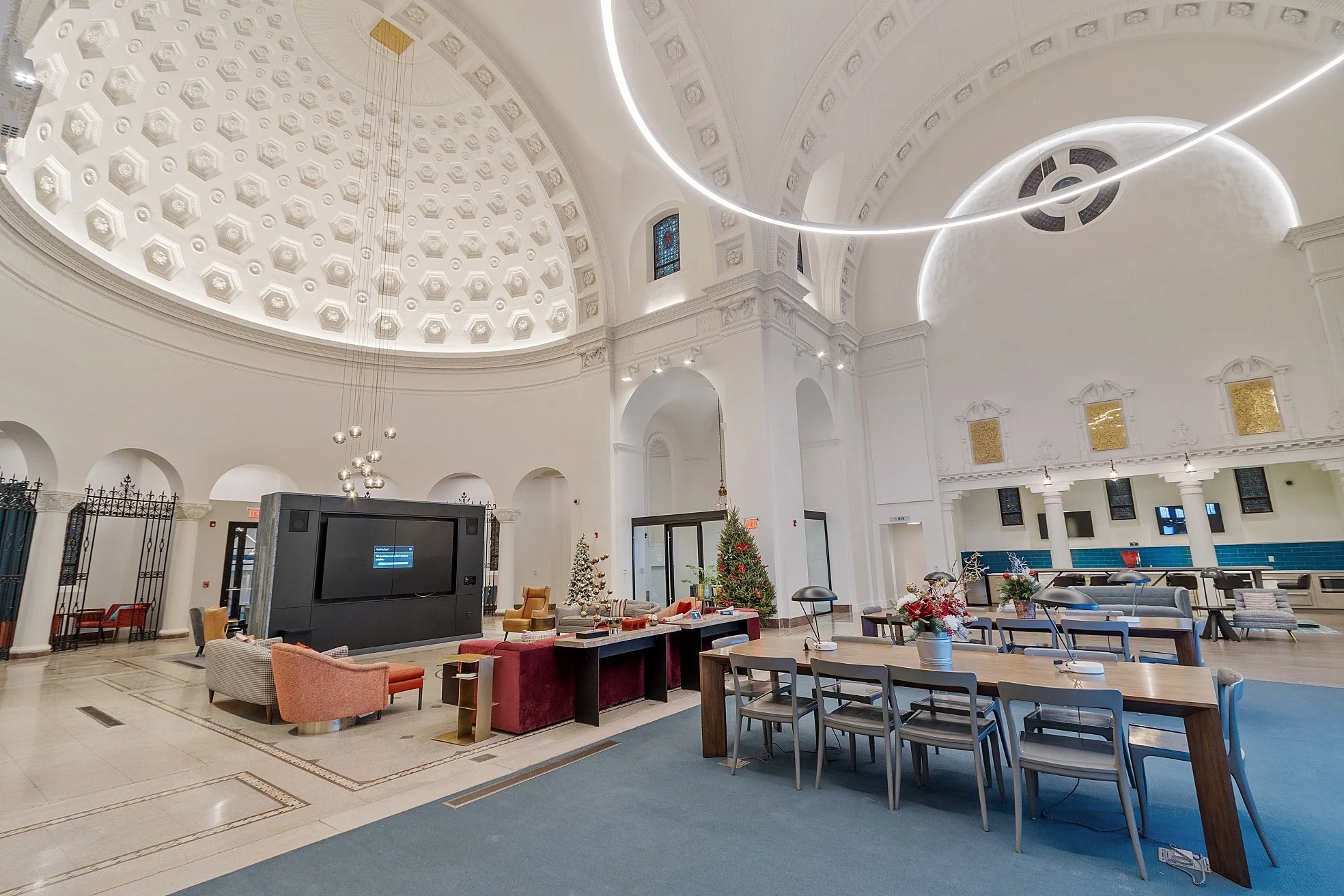 Interior of a spacious, white domed building decorated for Christmas with Christmas trees, festive decor, and modern lighting fixtures.