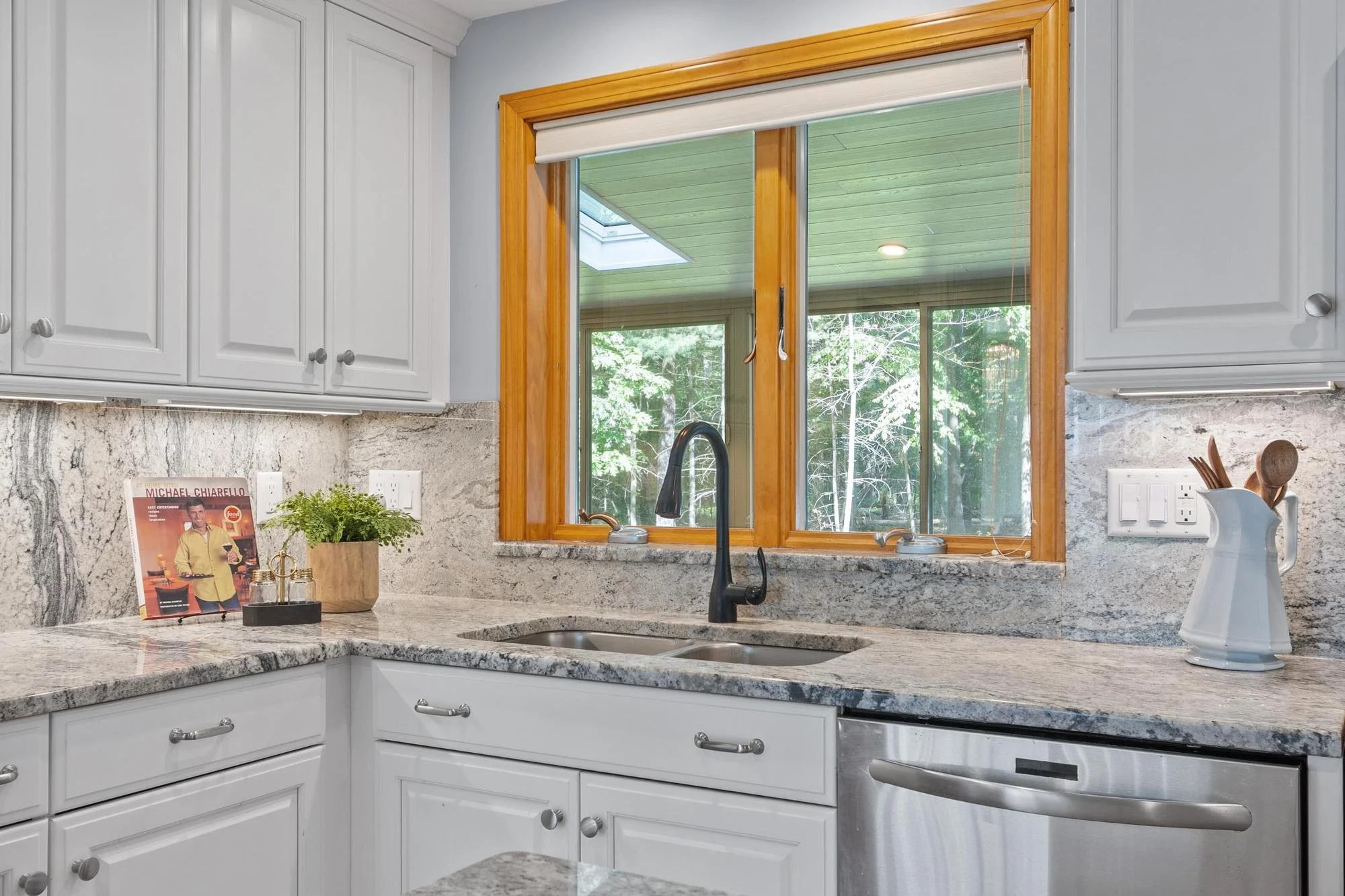 Kitchen with white cabinets, granite countertops, and a large window showing a view of a green backyard.