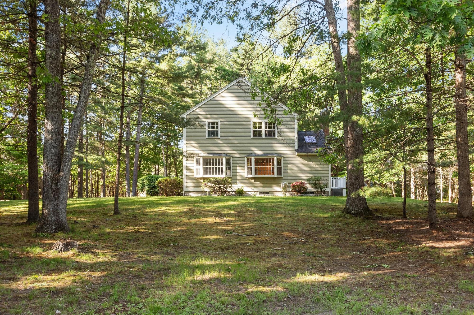 A house in a wooded yard with tall trees and a grassy lawn.