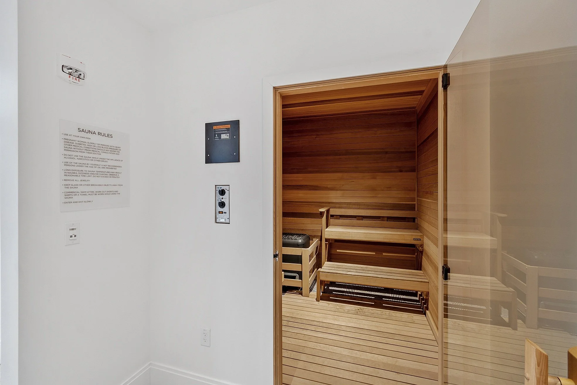 Indoor sauna room with wooden benches and a glass door located within a white wall area.