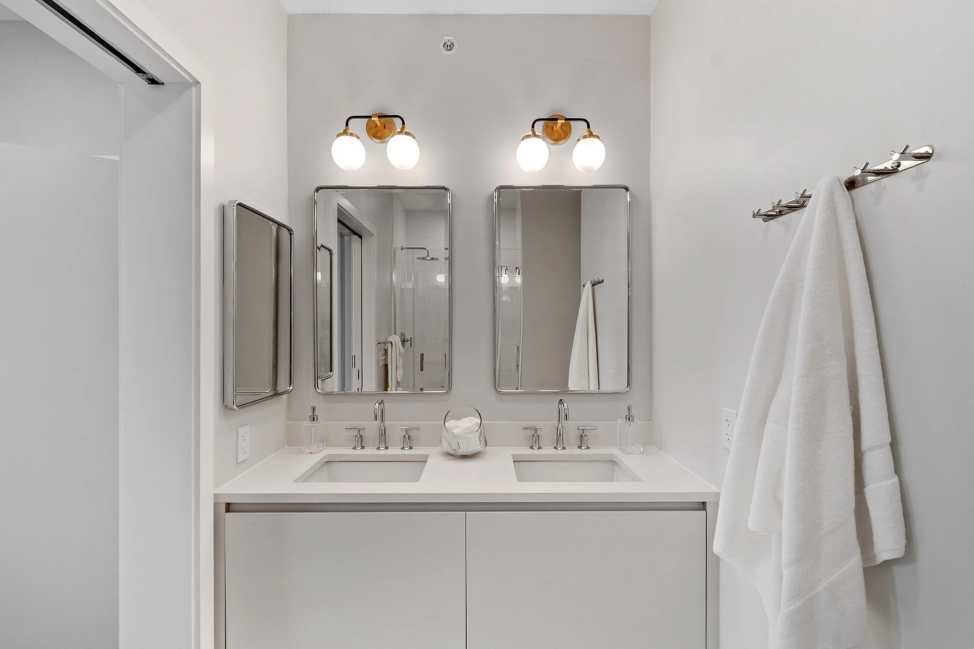 Modern bathroom with double sink vanity, two mirrors, wall-mounted lights, and white towels.