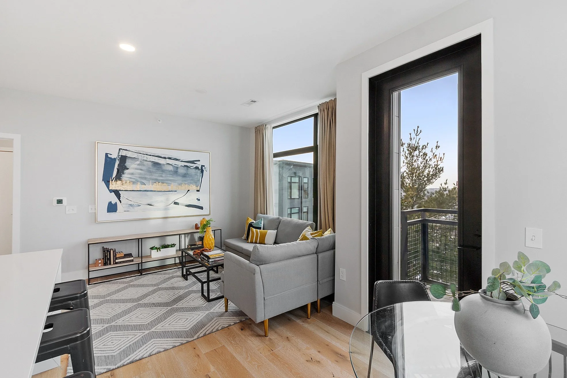 Living room with a sofa, abstract wall art, coffee table, and large windows with view of trees.