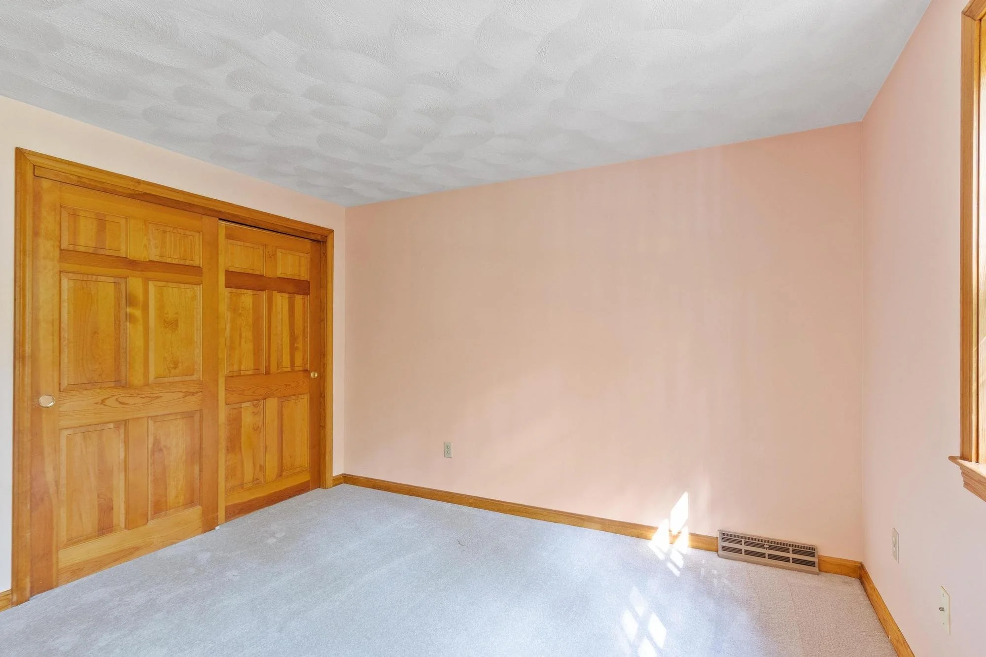 Empty room with beige walls, wooden trim, a closet with wooden sliding doors, a gray carpeted floor, and a floor vent near the baseboard.