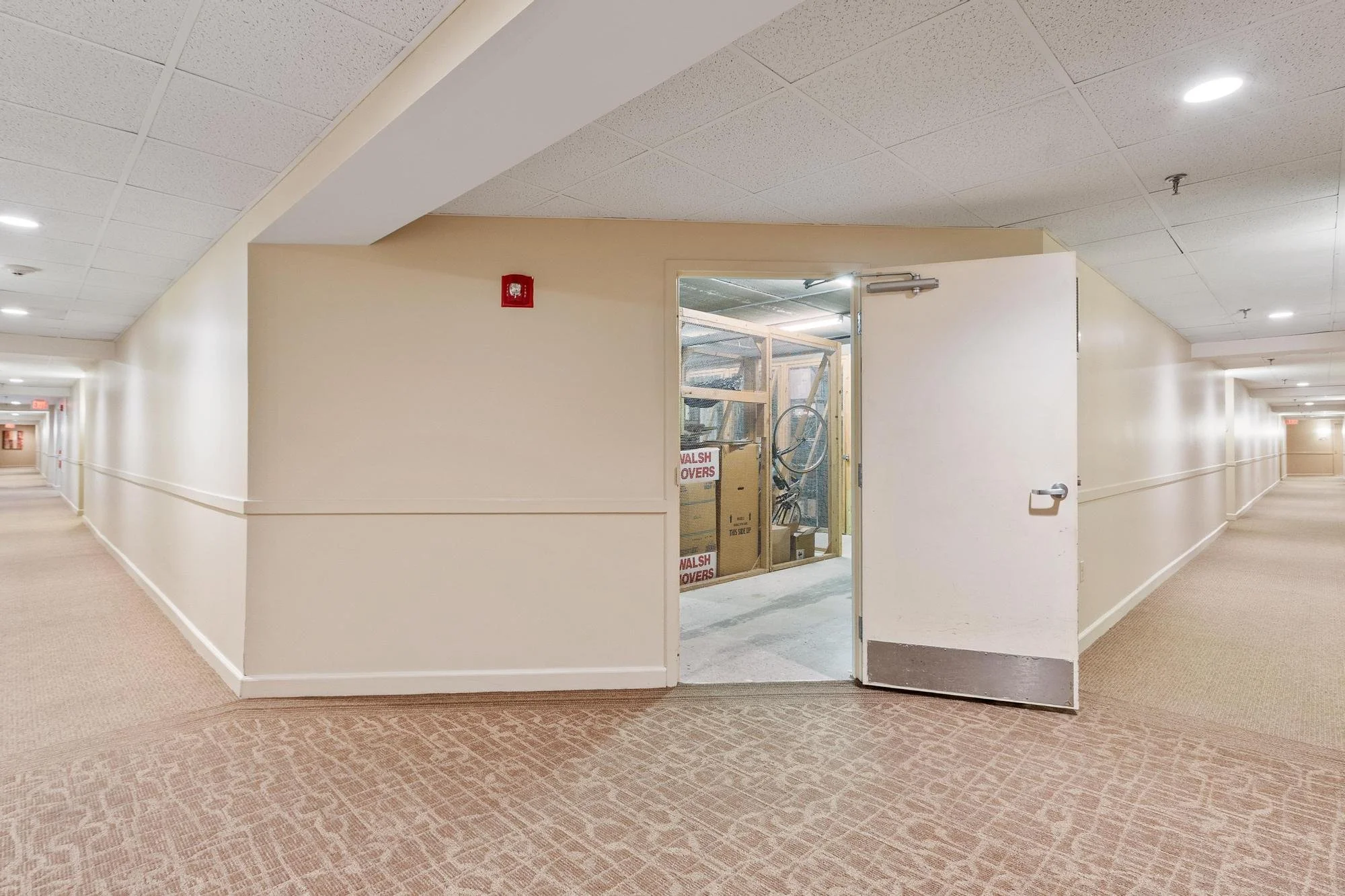 Hallway with beige walls and carpet, open door leading to construction area, ceiling with recessed lighting.