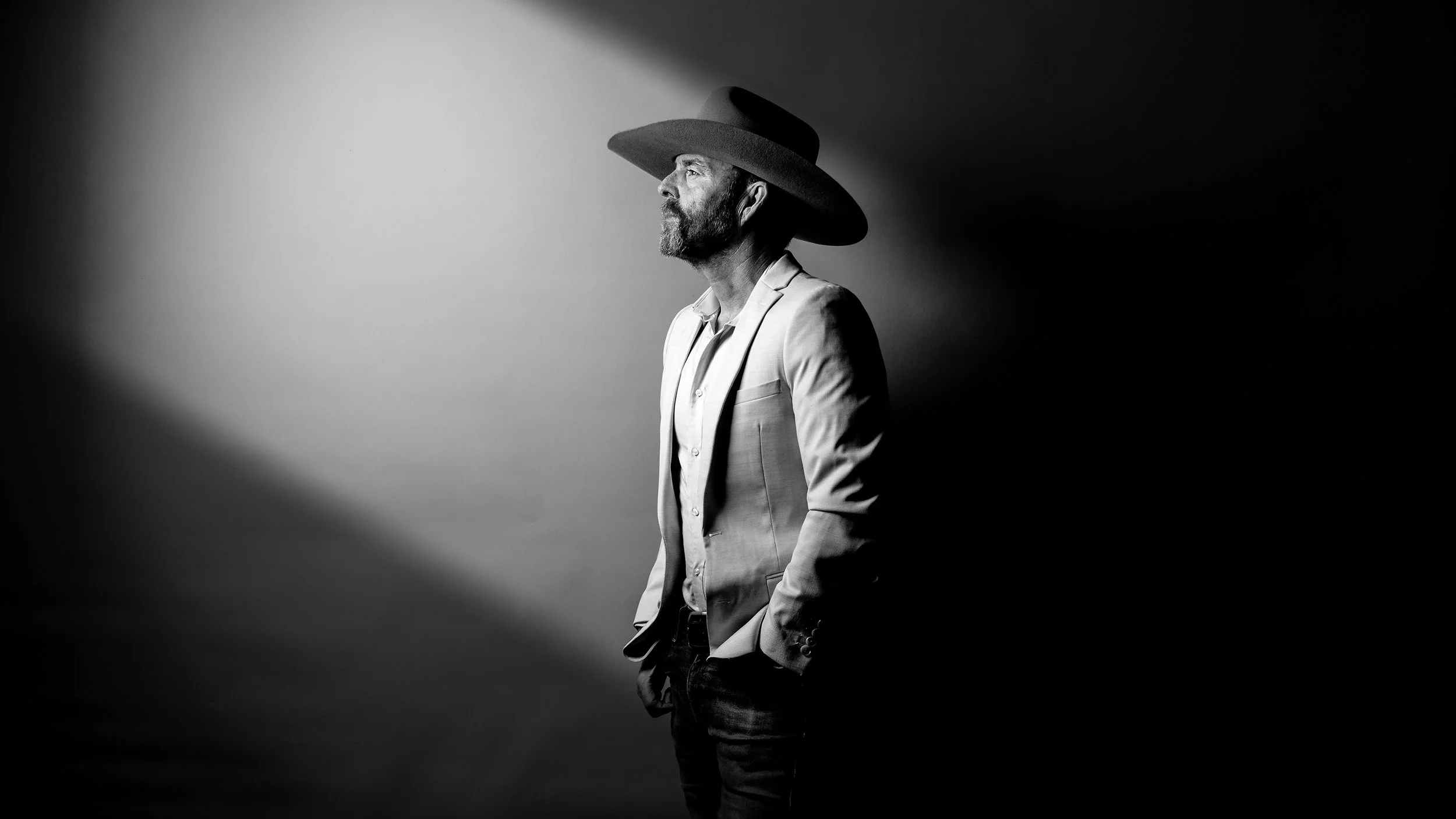 Portrait of Australian wine critic and photographer Campbell Mattinson, taken in 2026. Mattinson is wearing a suit, and a cowboy hat, in dramatic black and white lighting.