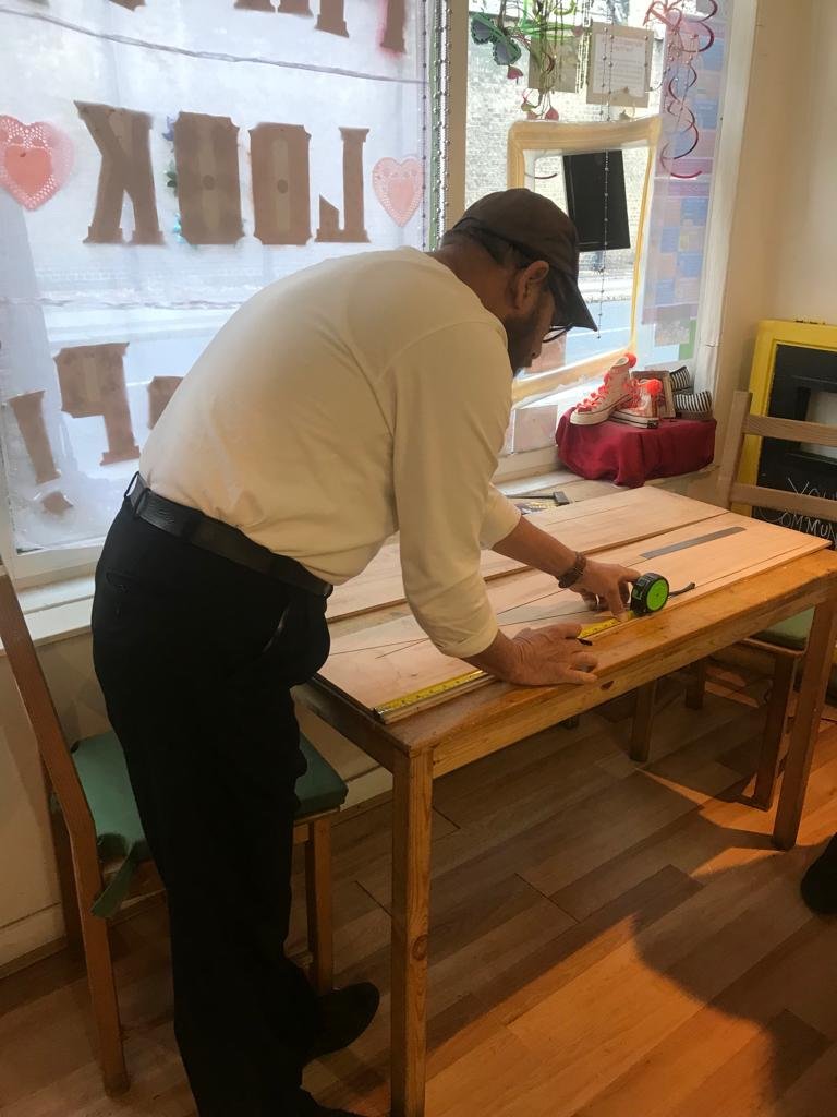 Man_measuring_wood_on_workbench.jpeg