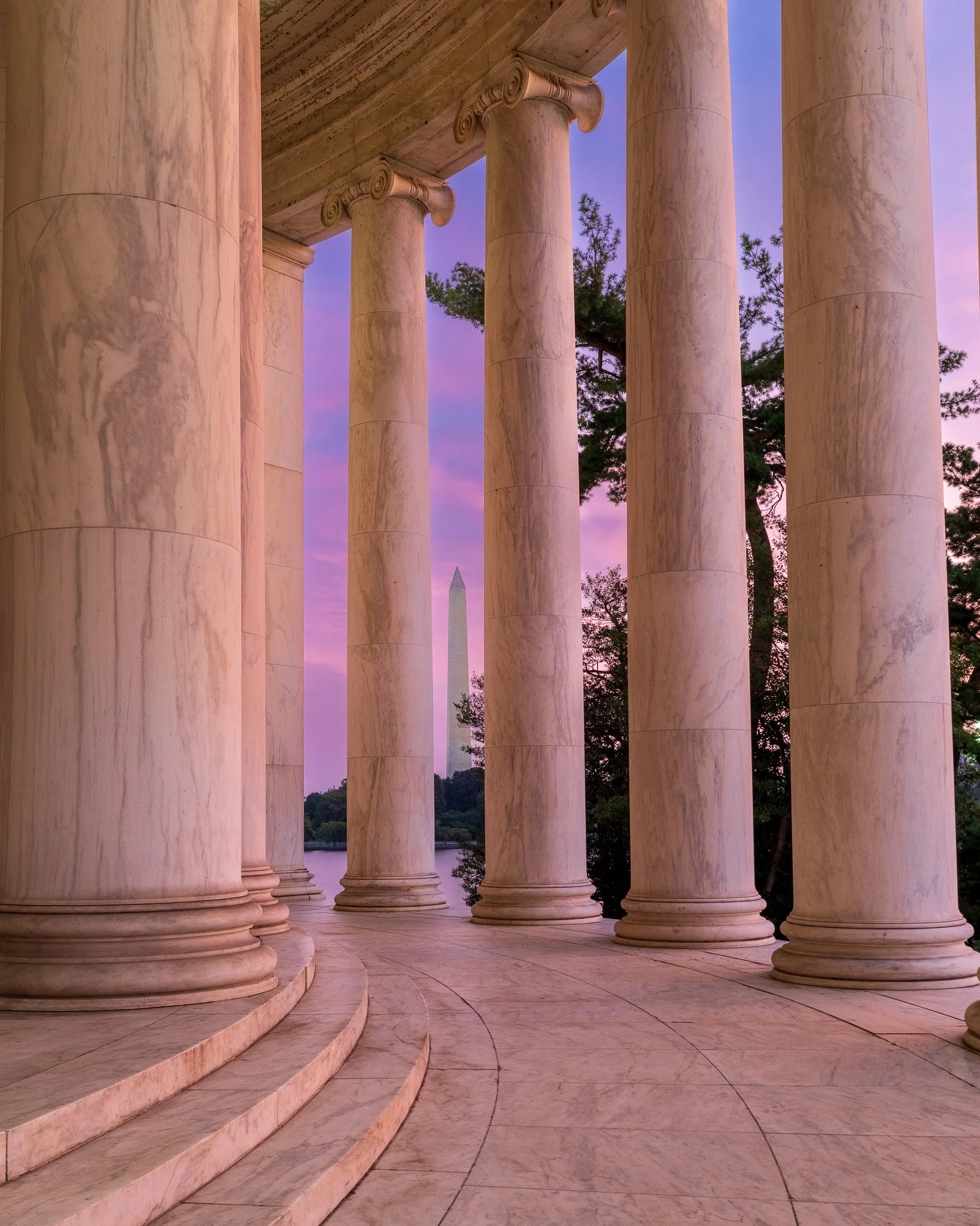 View of the Washington Monument seen through the columns of the Lincoln Memorial during sunset with purple and pink sky.