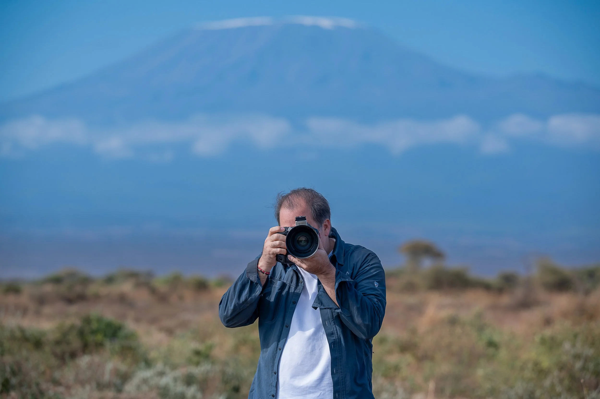 A person holding a camera up to their face, outdoors on a cloudy day.