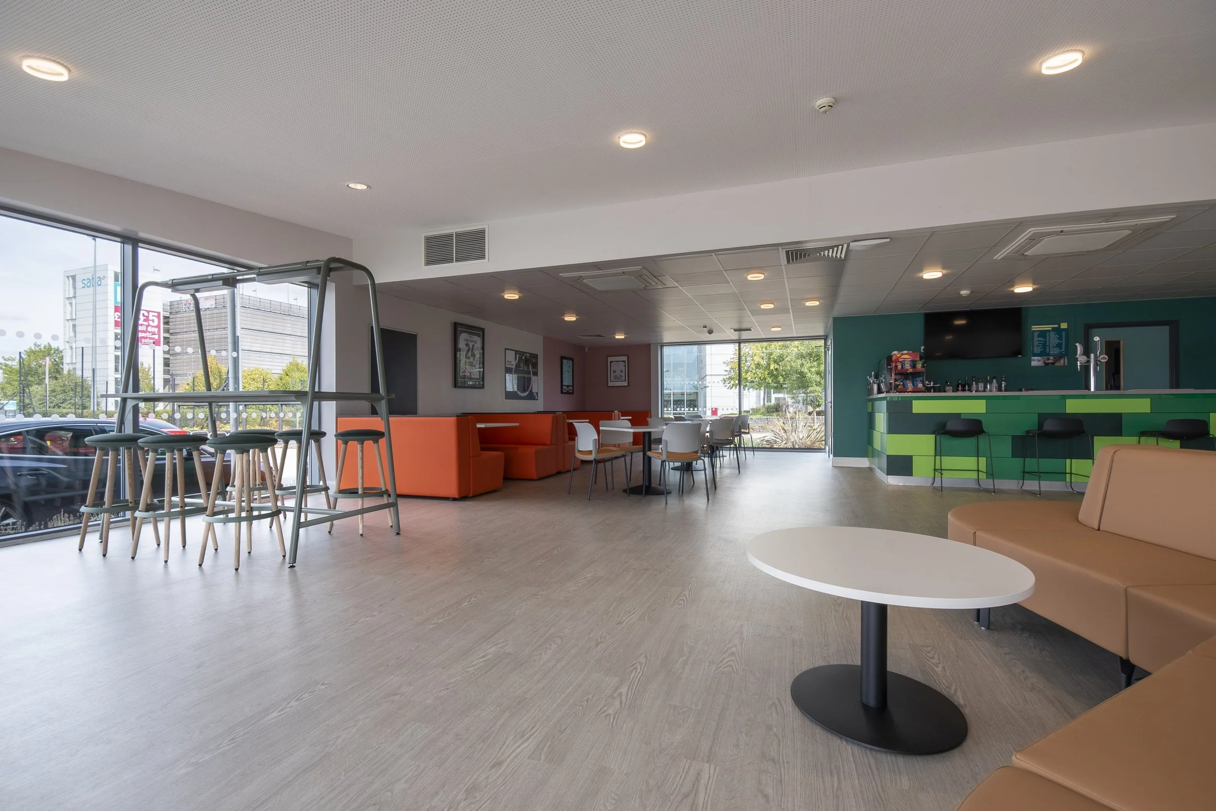 Wide view of the café with a round table, bench seating and green tiled bar