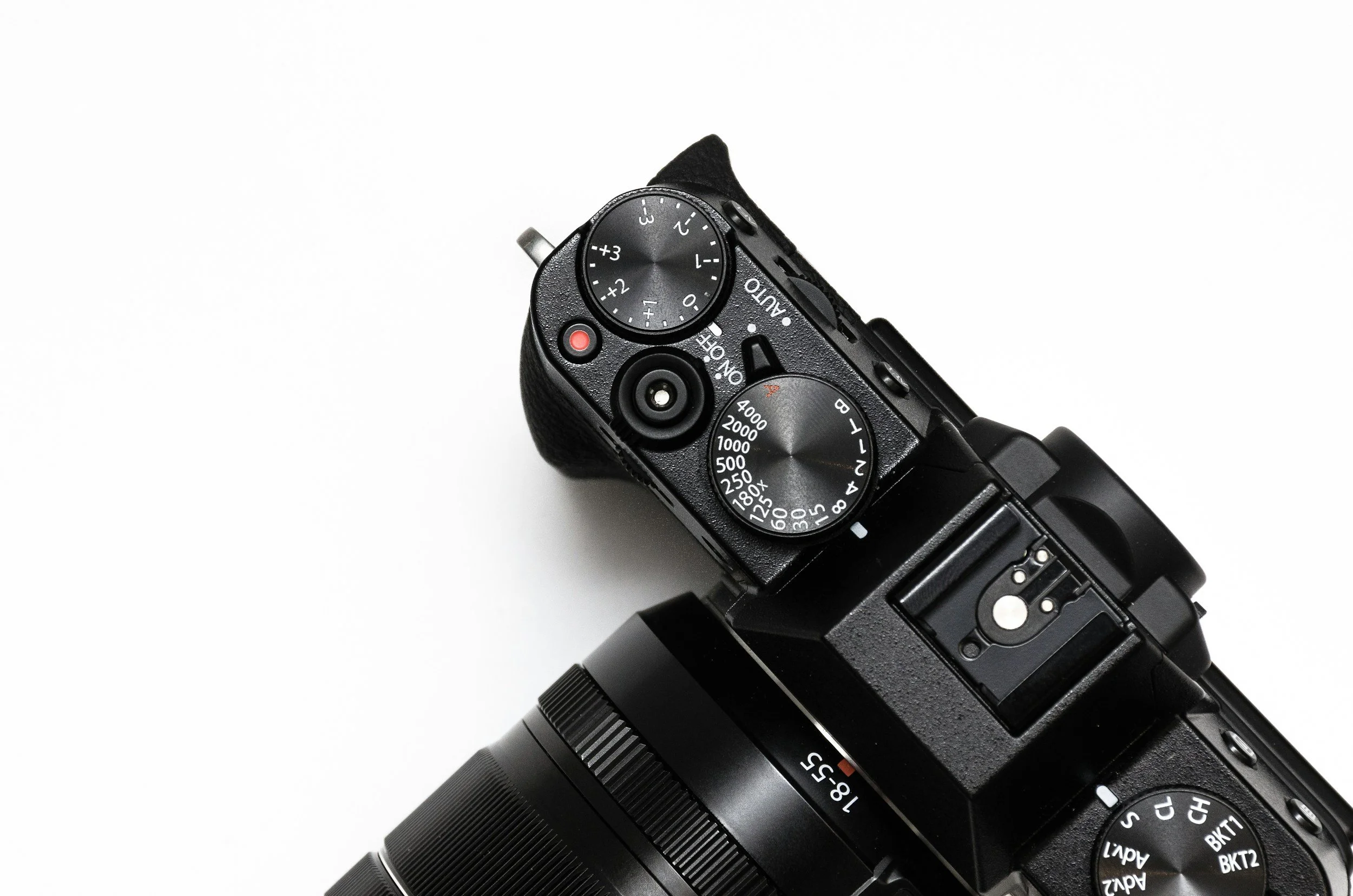 Close-up of a black digital camera with various control dials and a zoom lens, positioned on a white background.