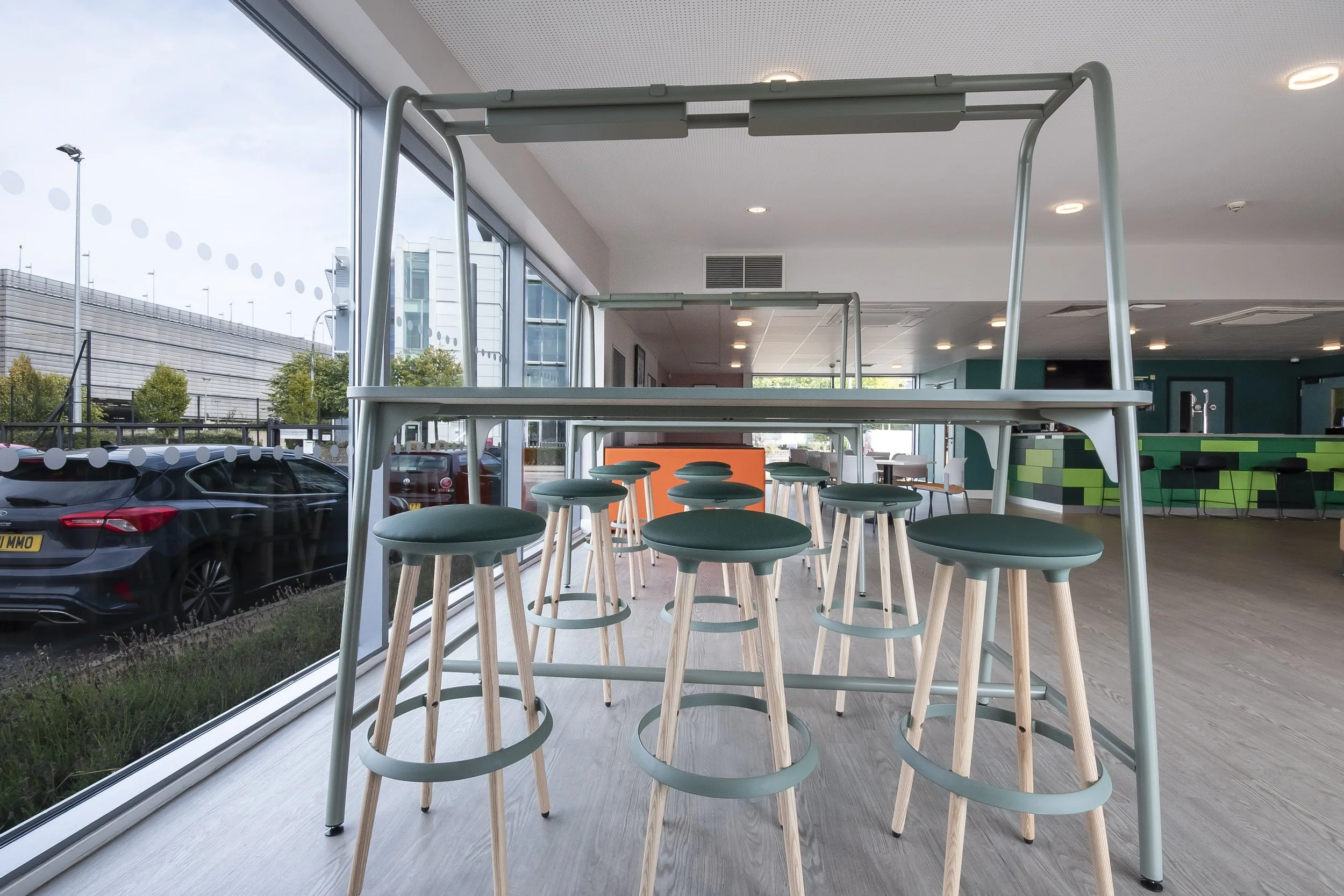 High table with green stools under a metal frame beside a window
