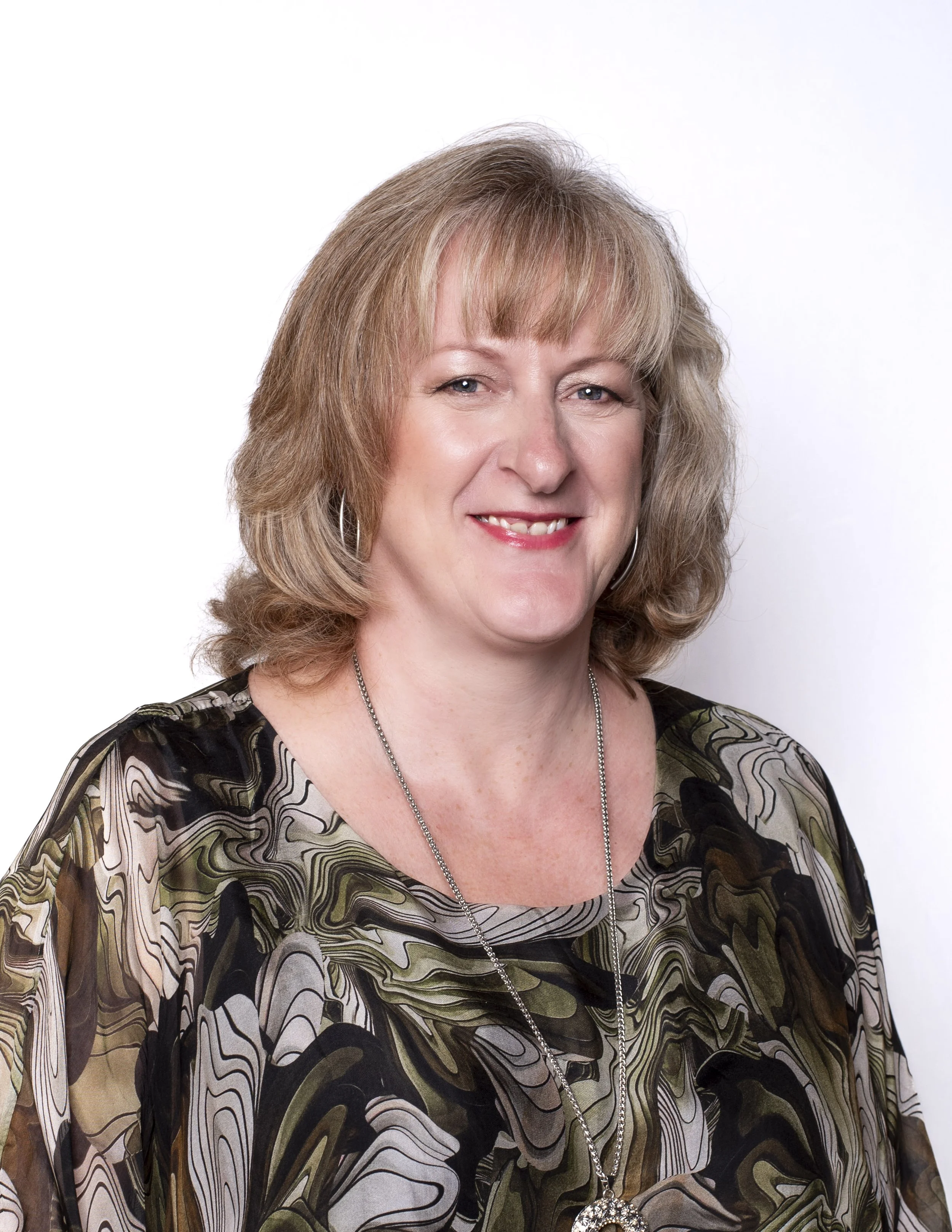 Headshot of a smiling woman with a blonde bob and a patterned top on a white background