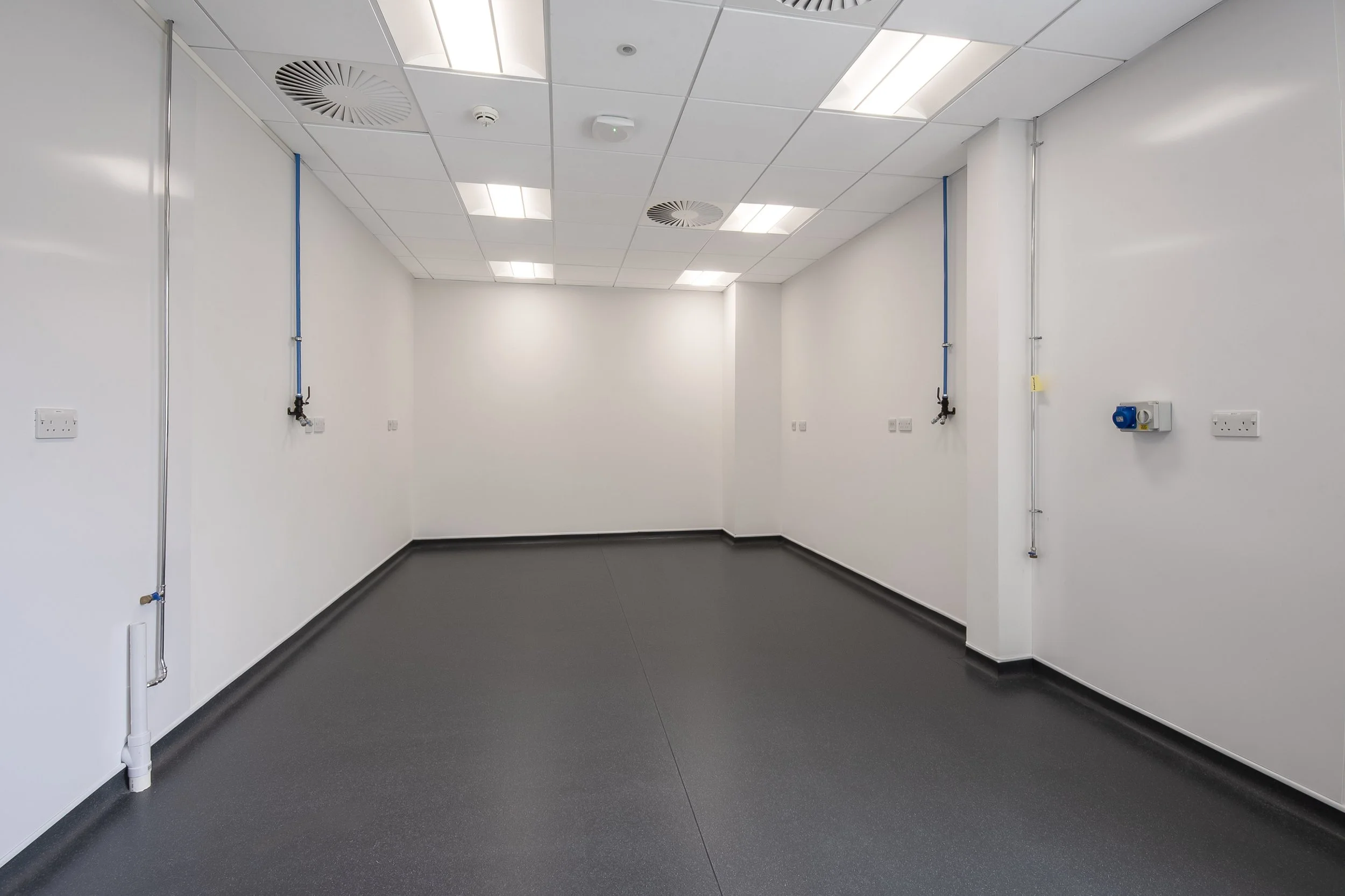 Empty white workroom with grey flooring and wall-mounted services