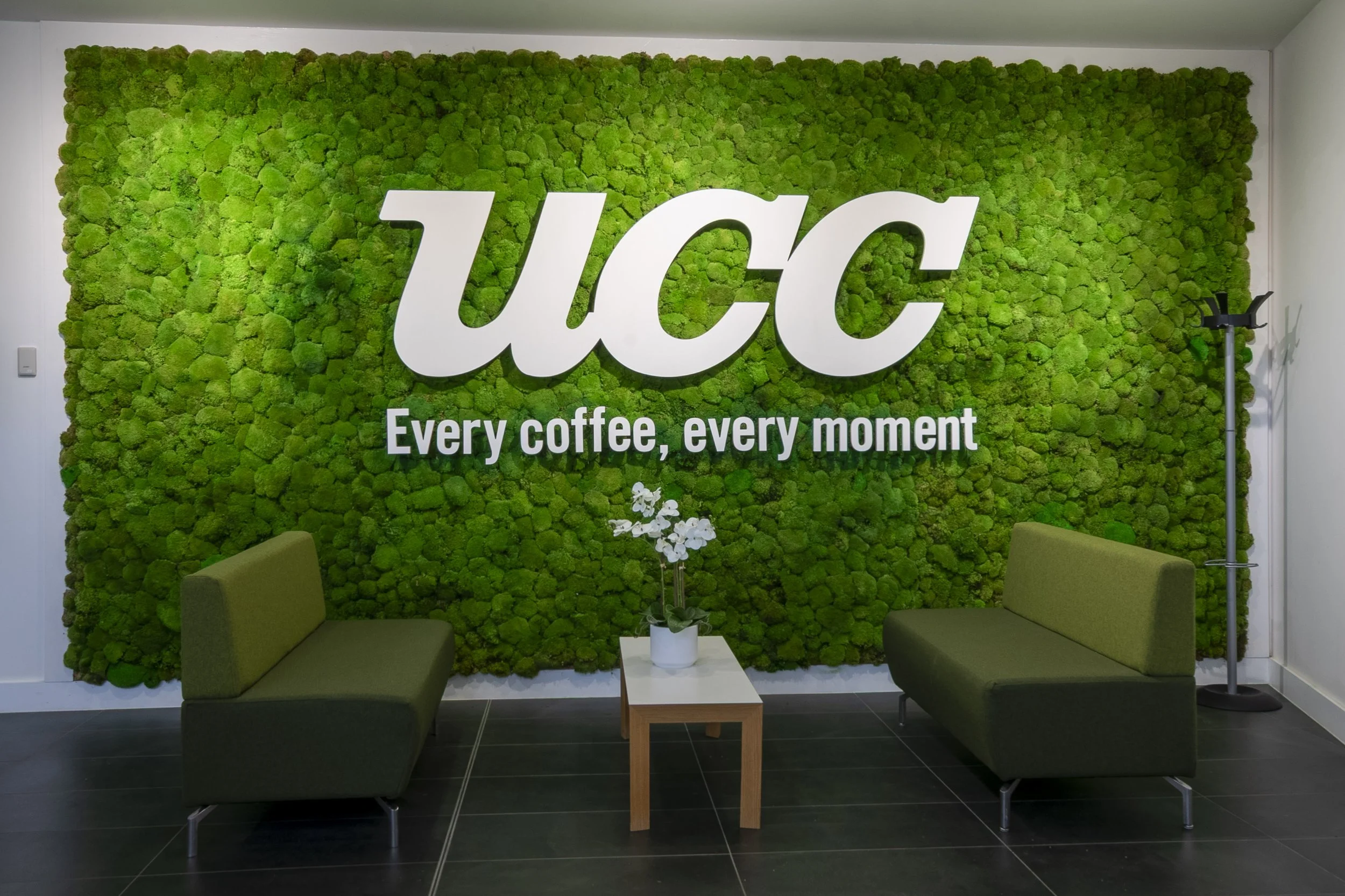 UCC logo on a green moss wall above two green armchairs in reception