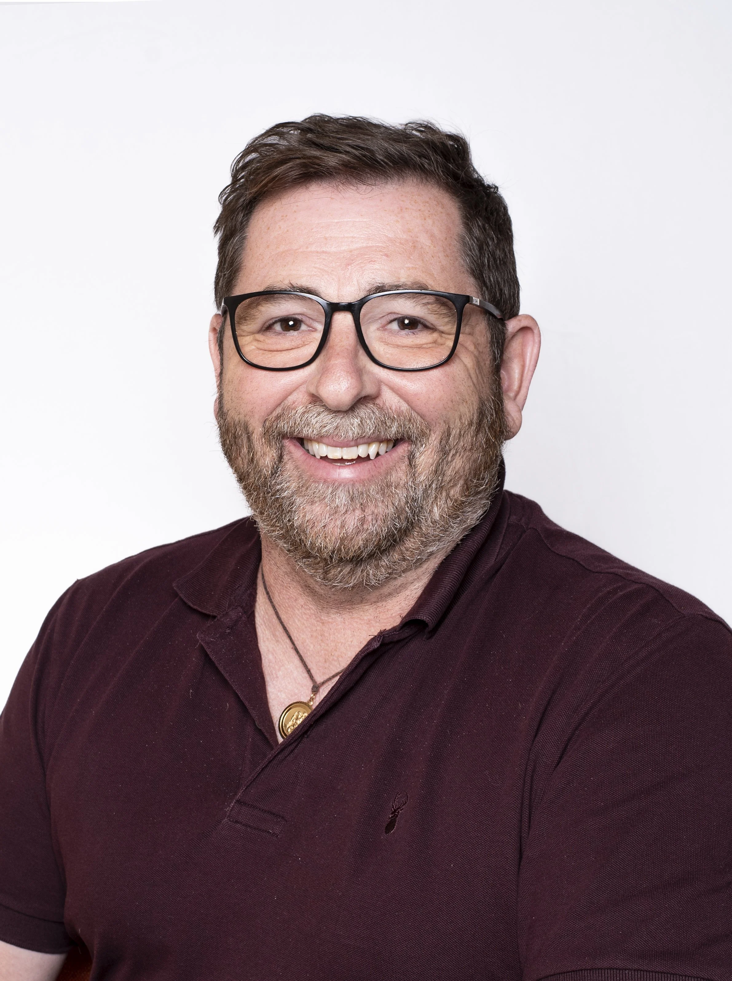 Close-up headshot of a smiling man with glasses and a beard in a burgundy shirt on a white background