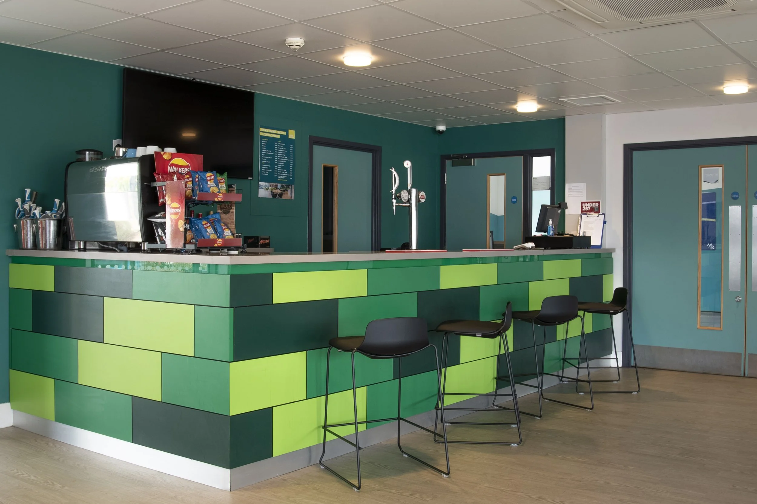 Green block-tiled bar counter with black stools and a wall-mounted TV